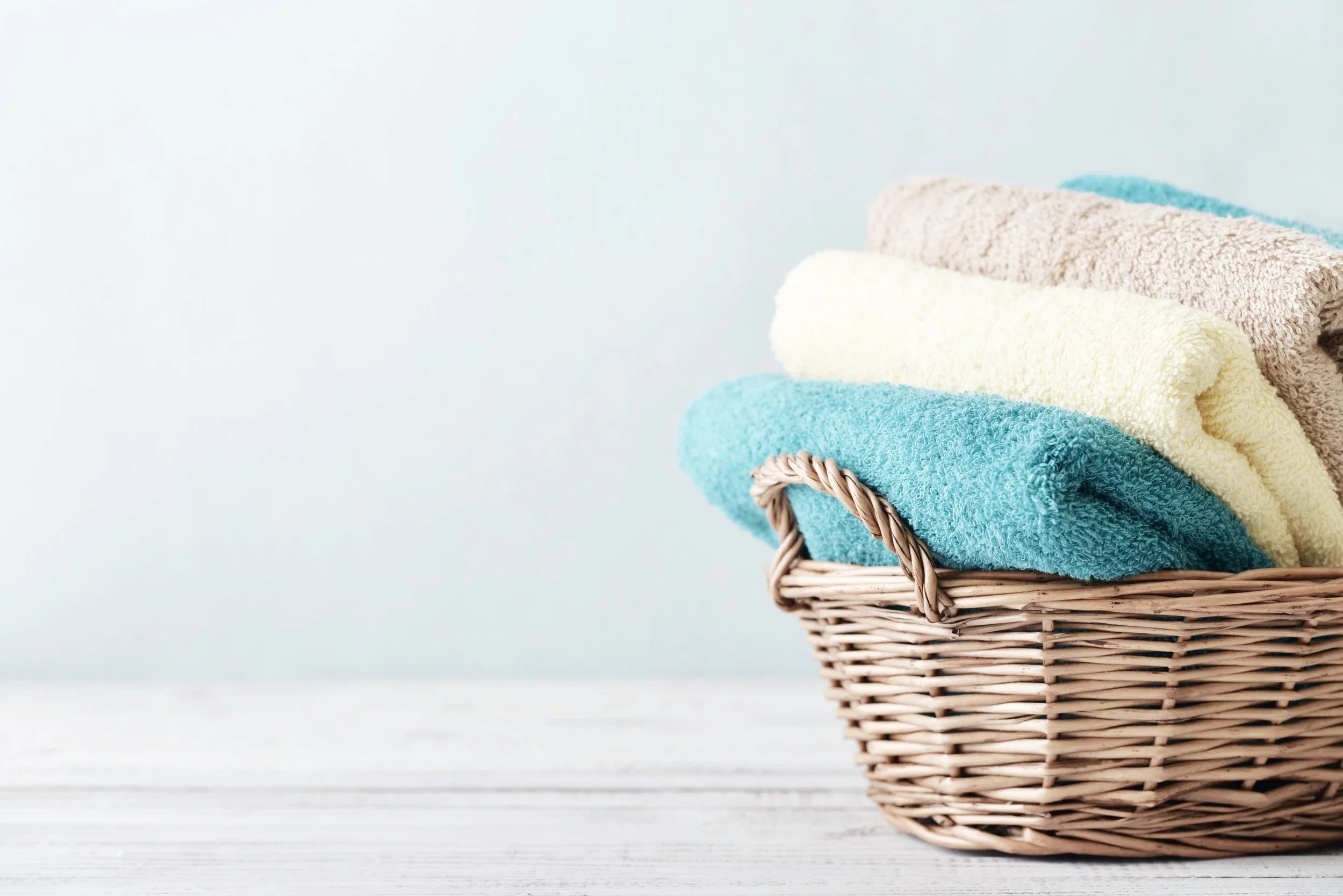 Stacked colorful towels in a wicker basket against a light background.