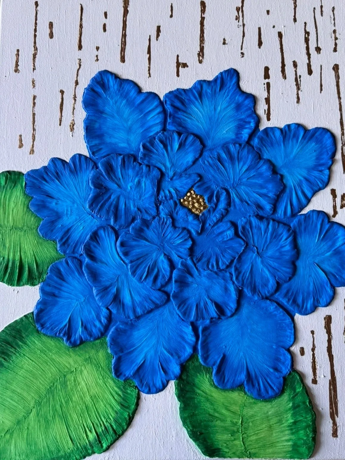 A close-up of a handmade art piece depicting a cluster of bright blue flowers with detailed petals, green leaves, and a small yellow flower with gold accents in the center, set against a white background with brown vertical lines.