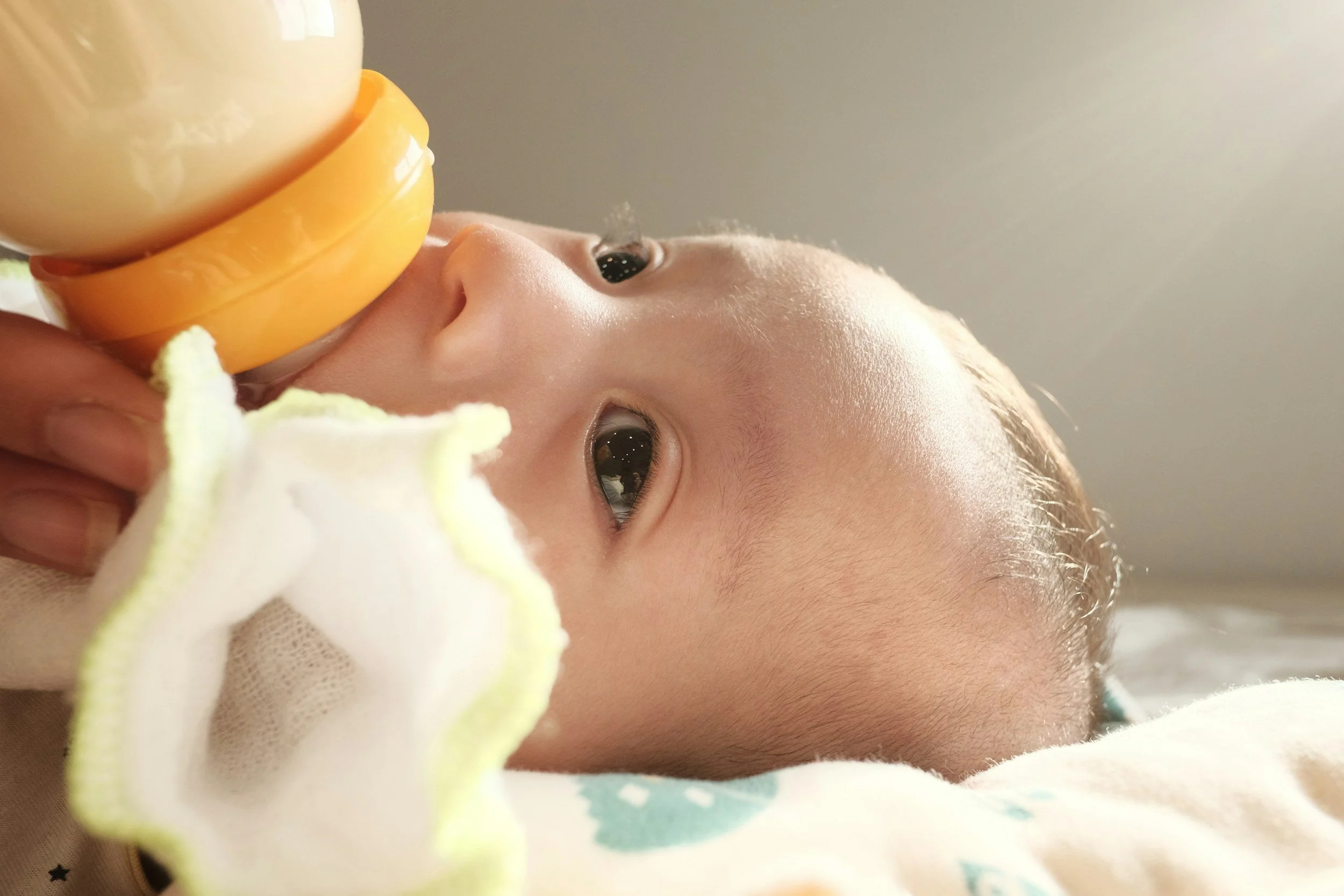 Close-up of a baby's face lying down, drinking milk from a bottle