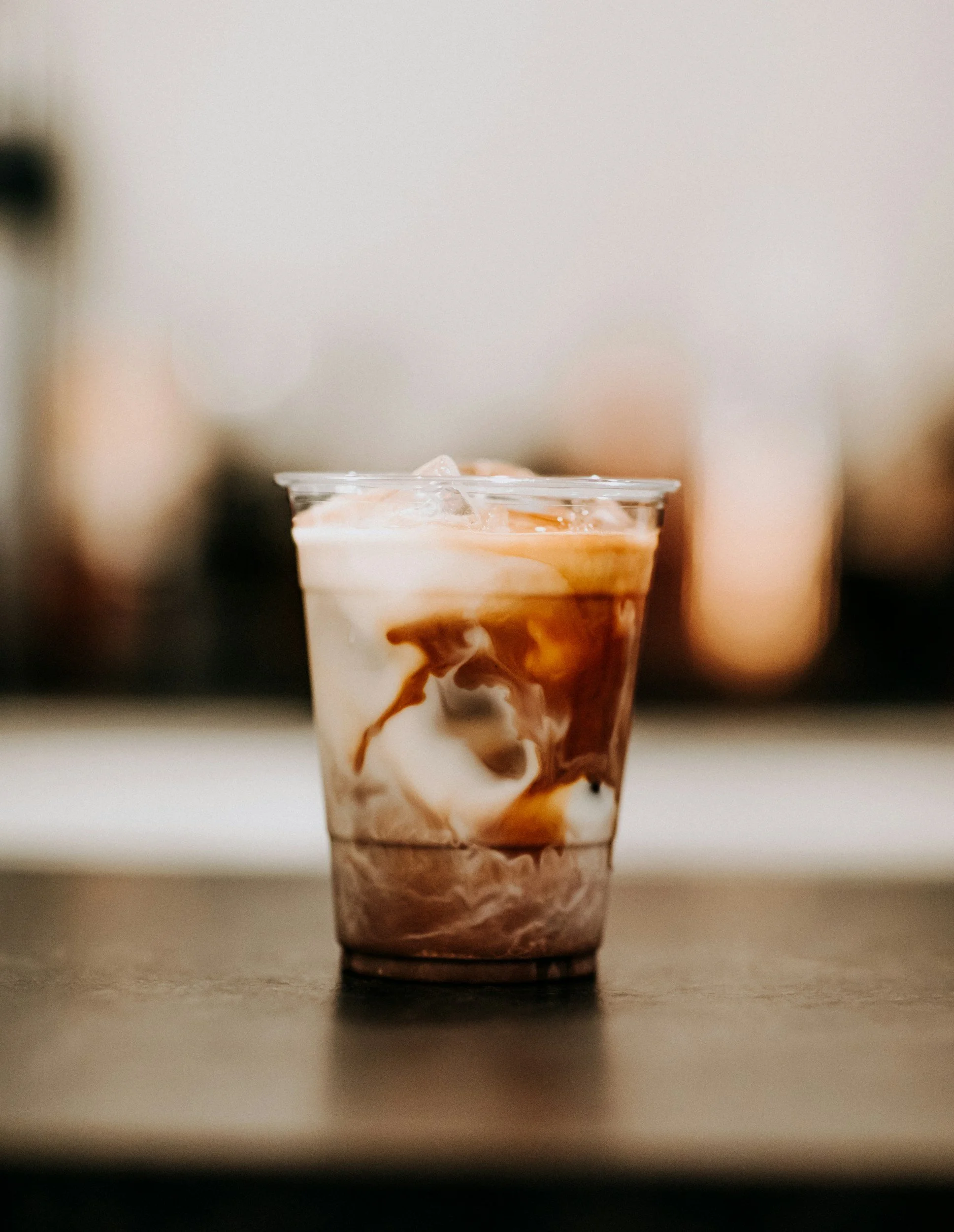 A close-up of a plastic cup with a layered drink, including swirls of caramel and cream, placed on a flat surface.