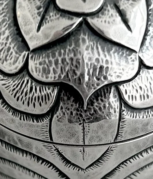 Close-up of a silver decorative object with intricate engraved patterns and a central symmetrical design.