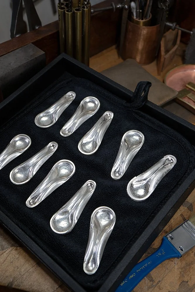 A black presentation case with ten silver objects inside, resting on a wooden surface.
