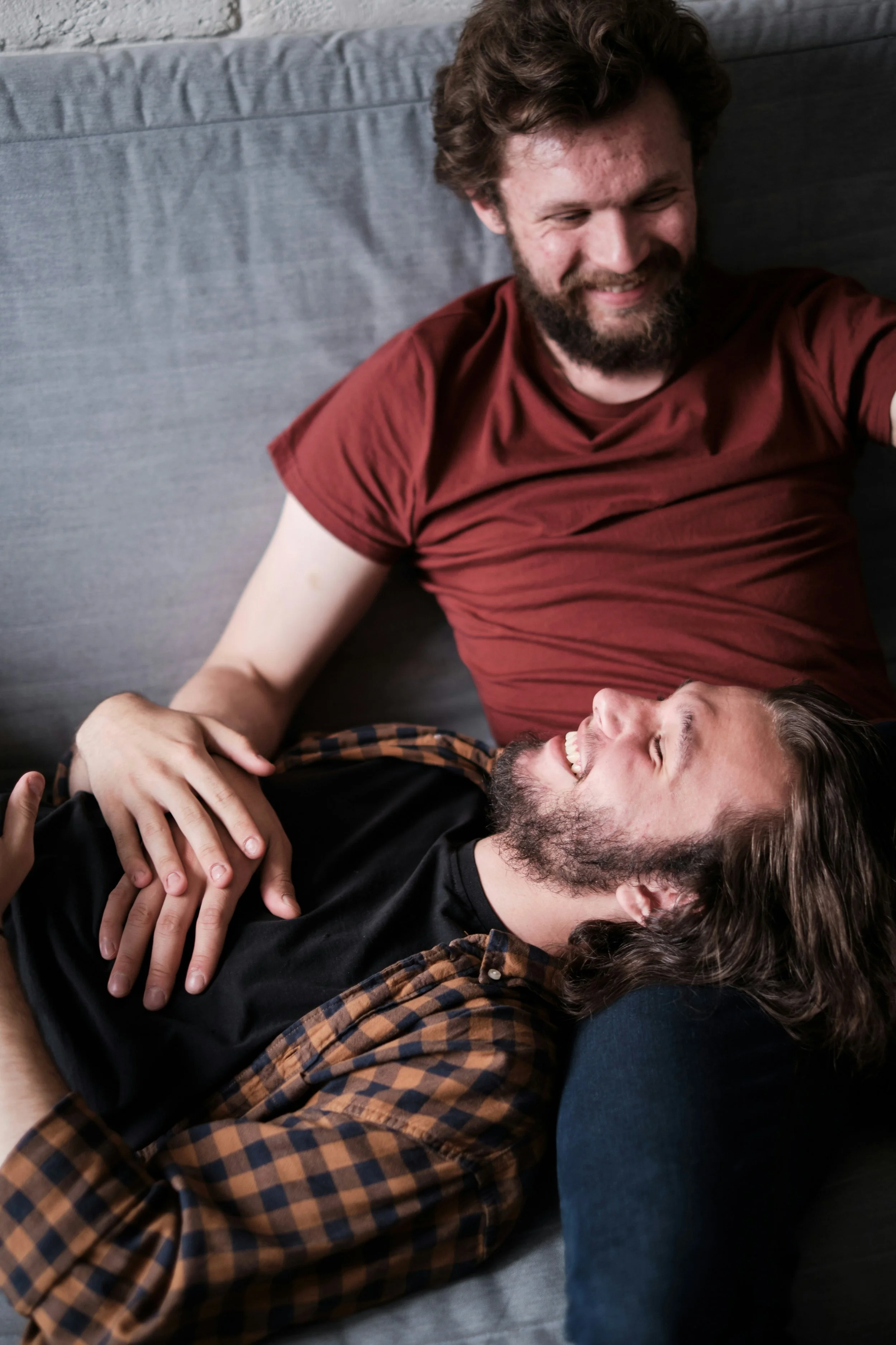 Two men lying on a couch, smiling and enjoying each other's company.