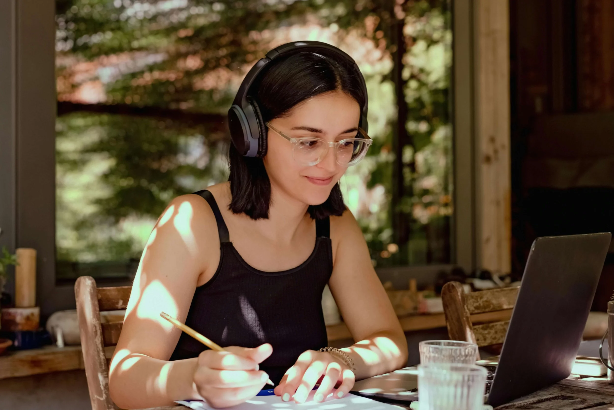 A woman with headphones takes notes in pencil.