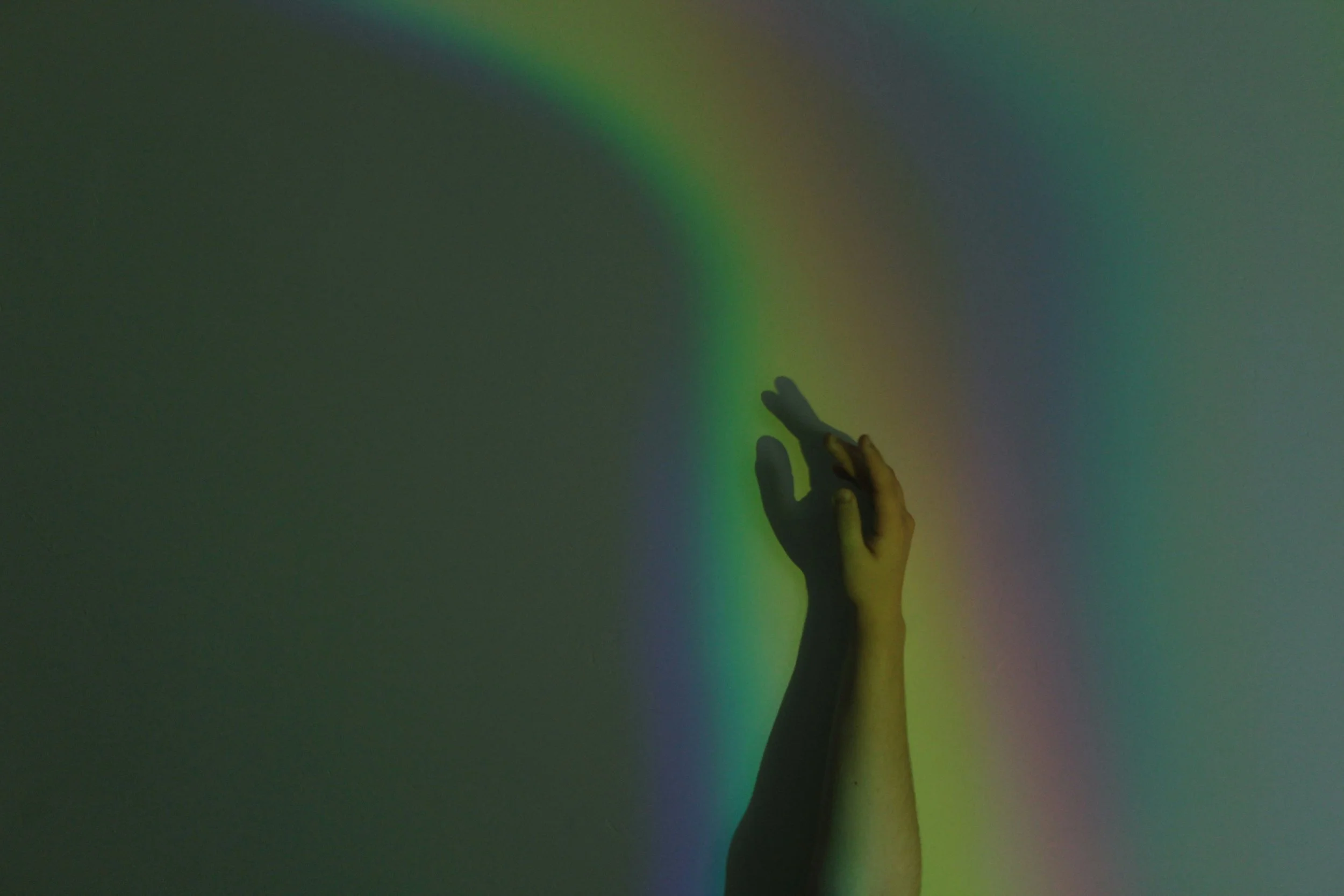 A hand reaching towards a wall with colorful light reflections creating a rainbow effect.