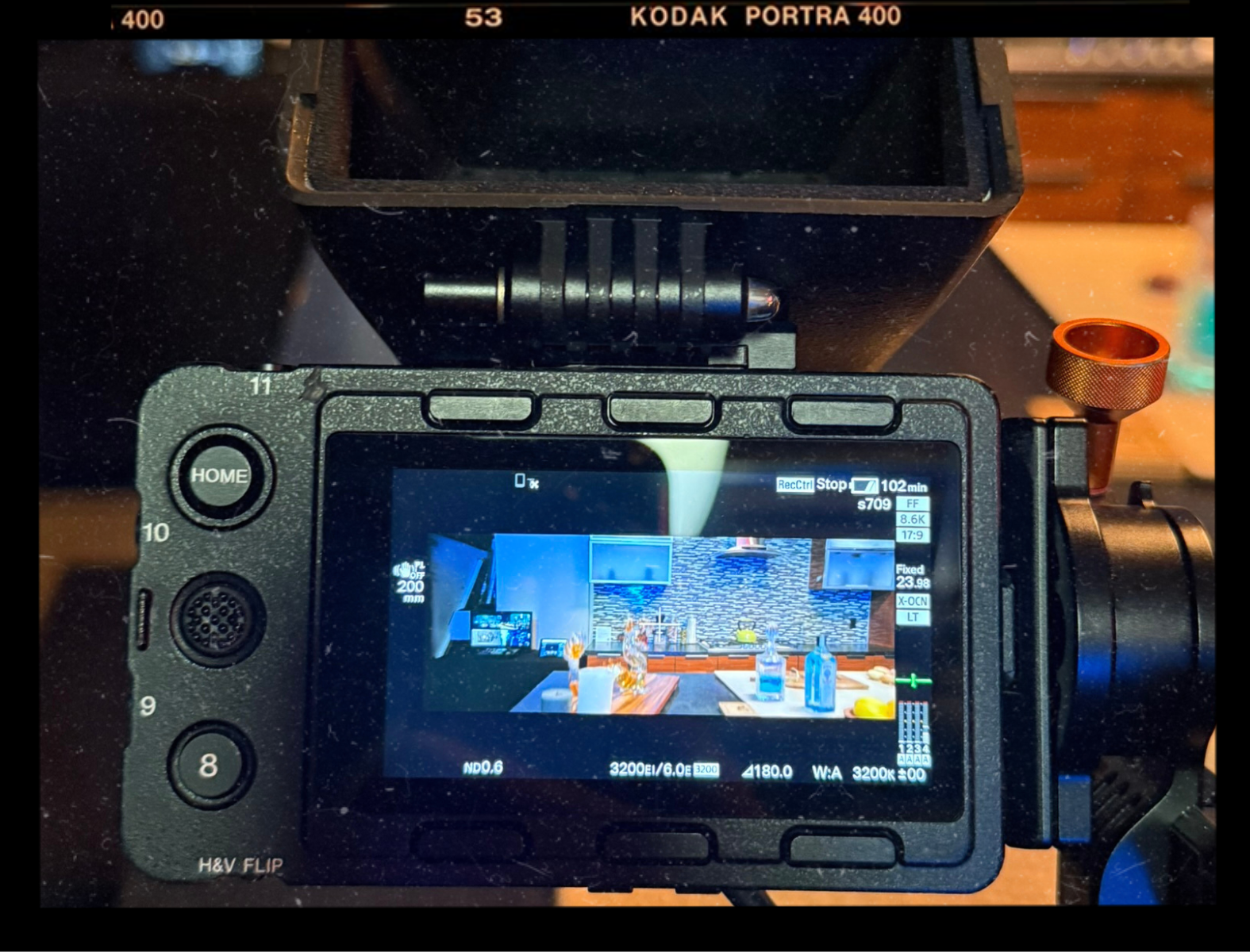 A digital camera's screen displaying a setup on a film set. The camera is pointing at a scene inside a room, with various objects and a textured wall in the background.