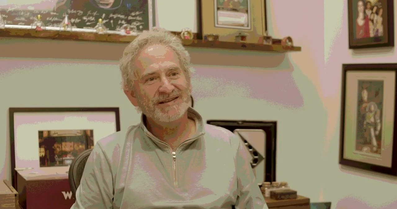 A man smiling in a room decorated with framed artwork and collectibles on the shelves.