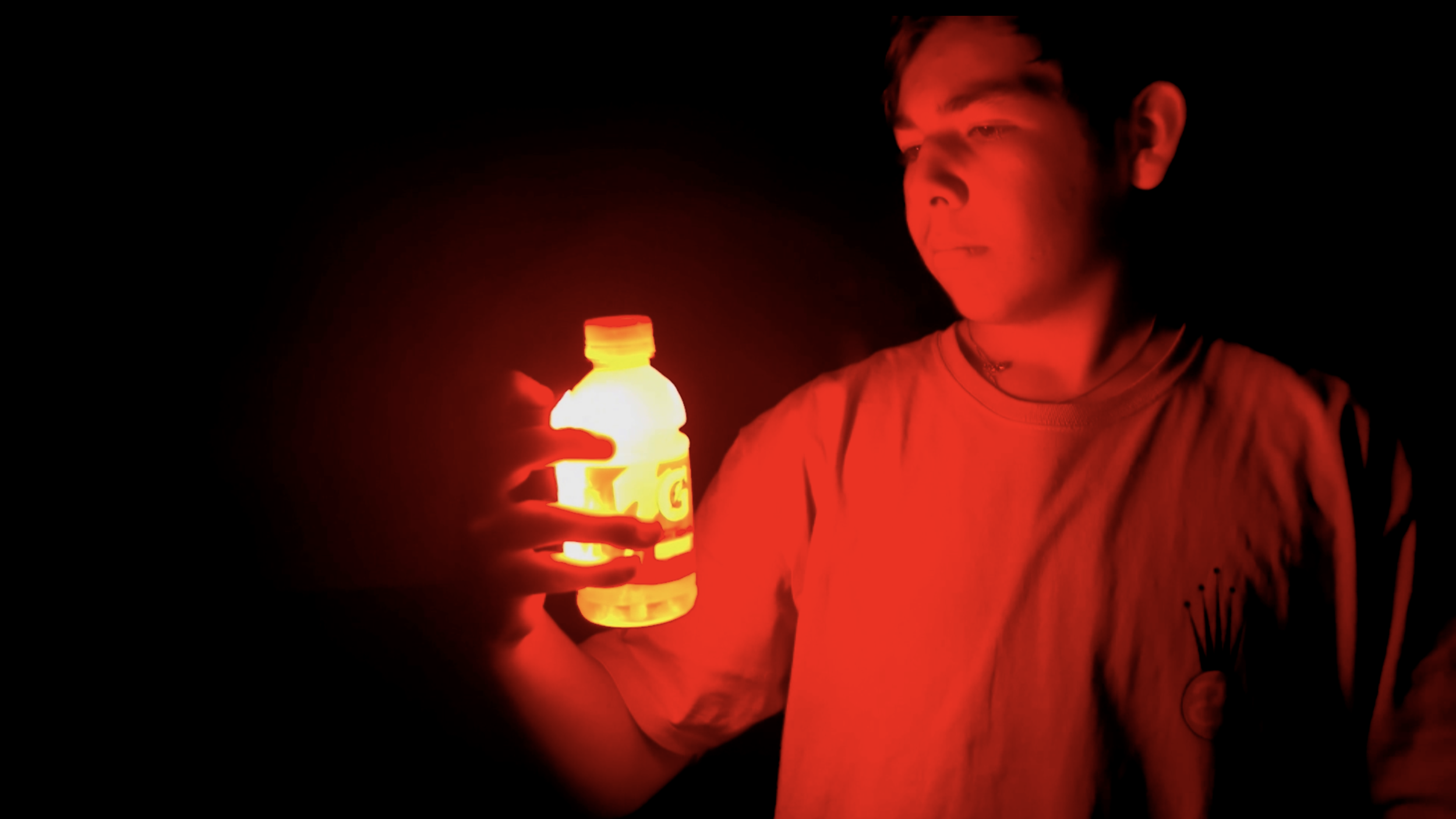 A person holding a glowing yellow-orange bottle in a dark environment, illuminated by the bottle's light.