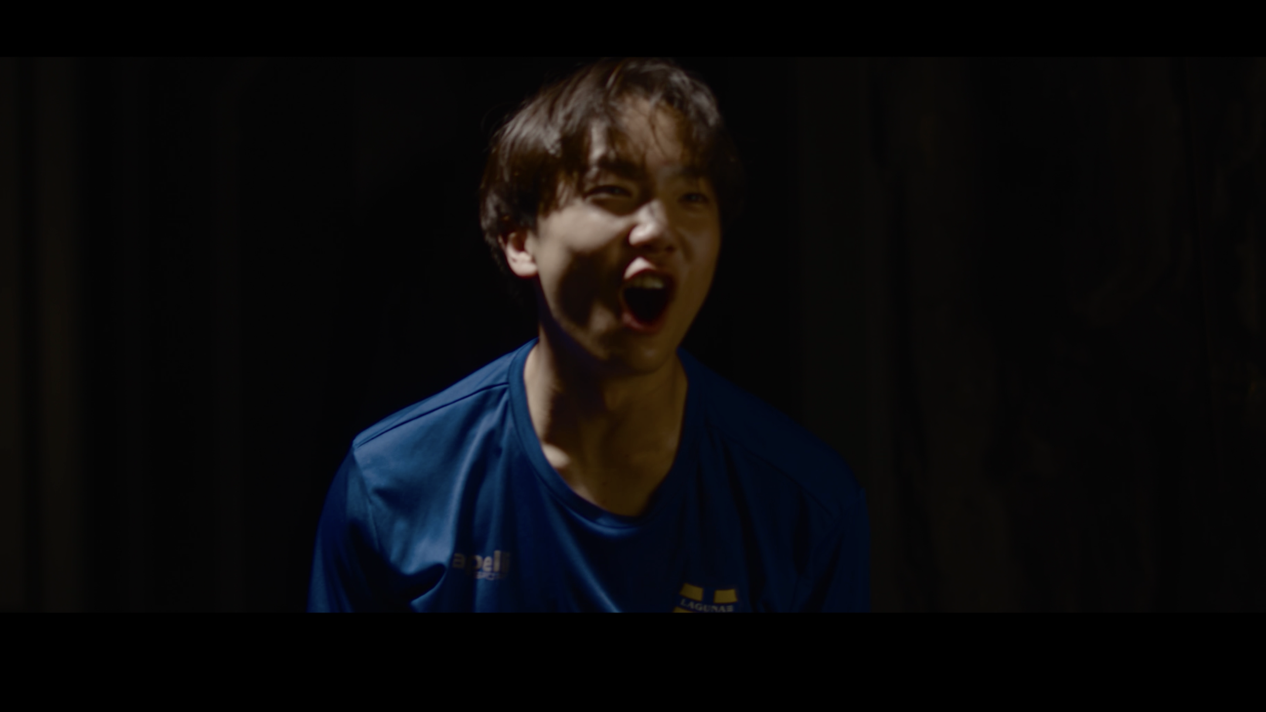 A young man with brown hair in a blue sports jersey, shouting or celebrating with an intense expression.