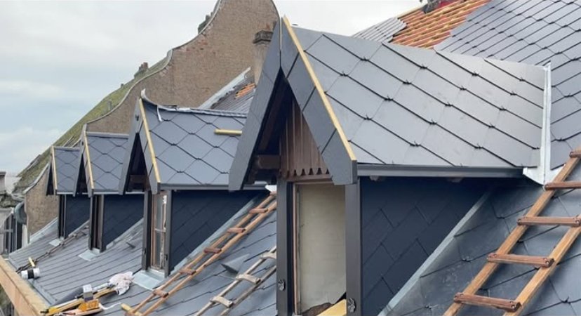Travaux de rénovation sur un toit en ardoise avec plusieurs fenêtres de toit en cours d'installation.