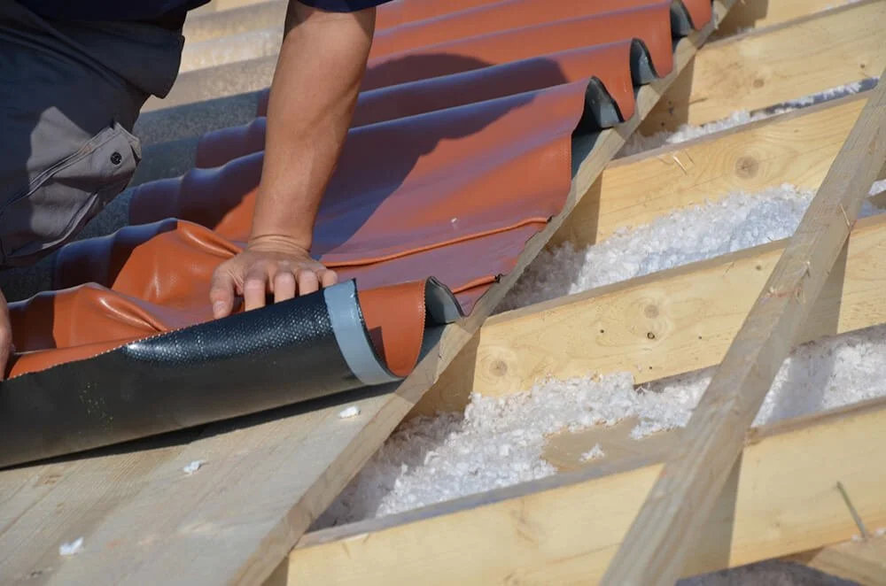 Person posant une membrane d'étanchéité sur une structure en bois lors de la construction d'un toit.