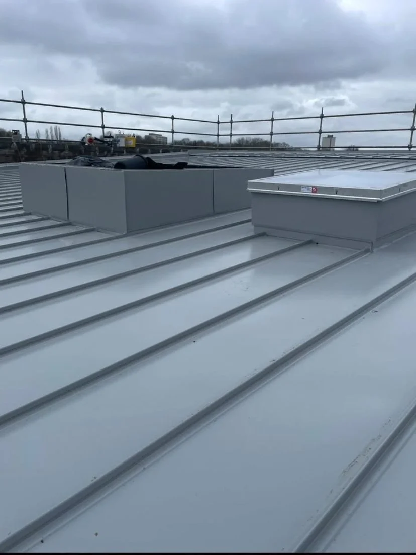 Vue d'un toit en métal avec des ventilation et des dispositifs de collecte d'air, sous un ciel nuageux, avec une structure de sécurité en haut.