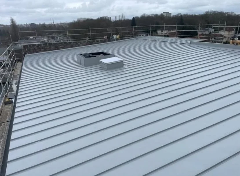 Toit en métal en pente avec des cheminées et une cheminée de ventilation sur un bâtiment.