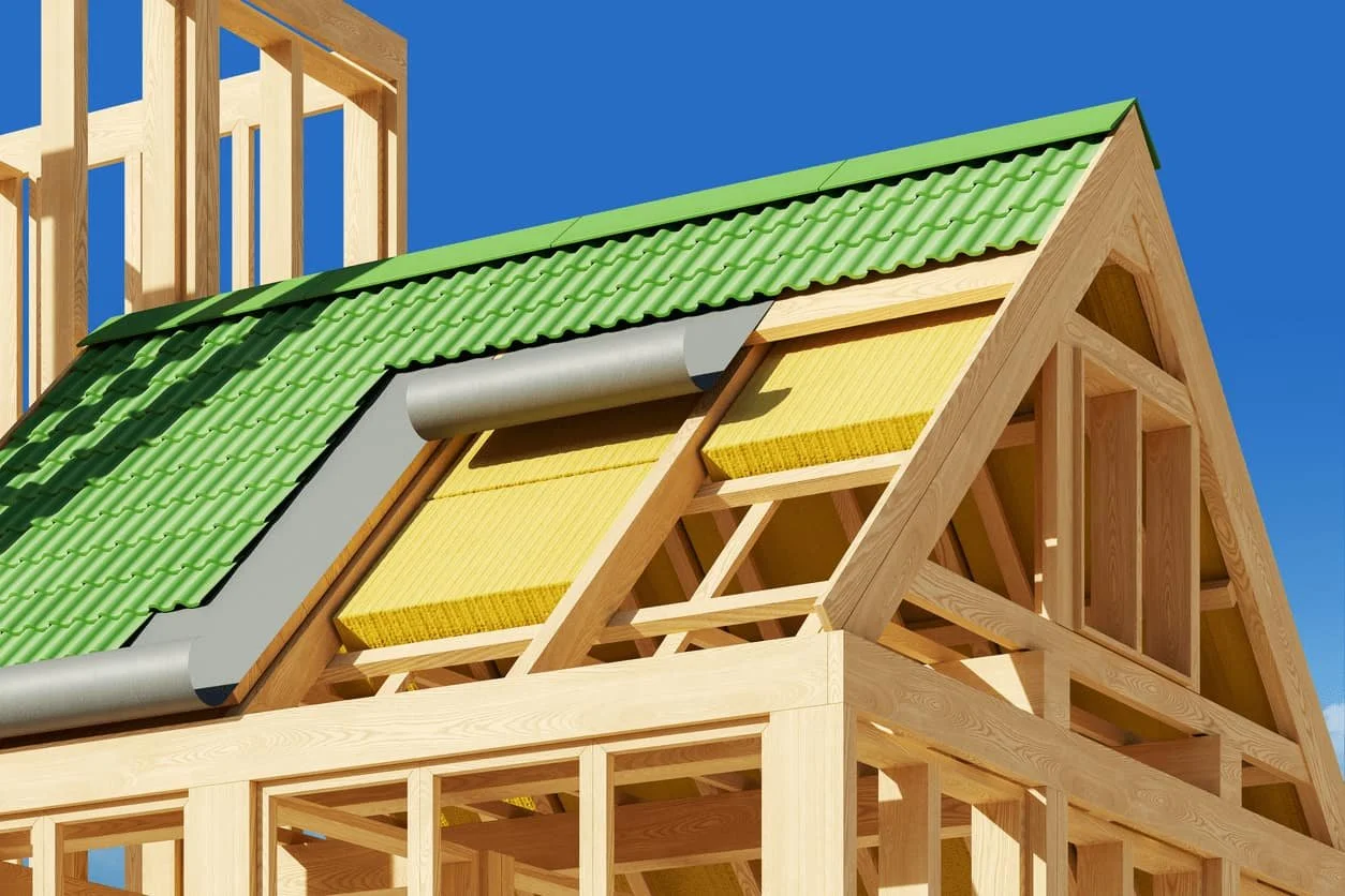 Construction d'une maison en bois avec un toit partiellement couvert de tuiles vertes et une partie en isolation jaune. La structure en bois, le toit en construction et un ciel bleu en arrière-plan sont visibles.