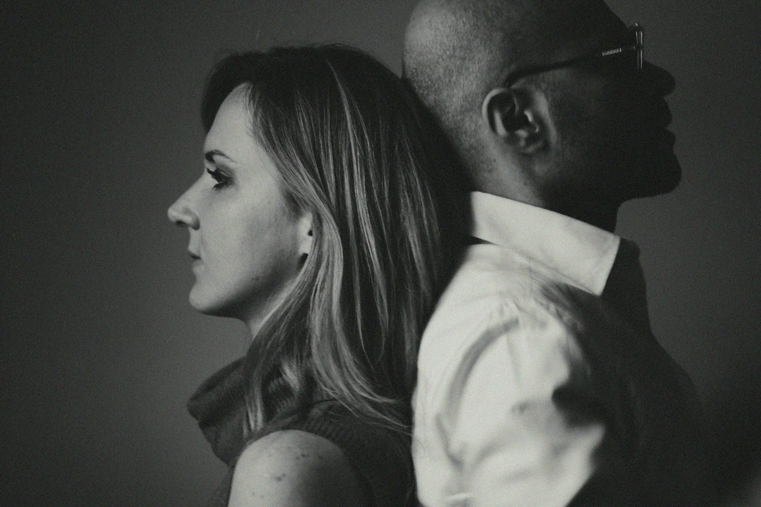 Side profile of woman with long hair and man with glasses and buzz cut, both facing opposite directions, black and white photo.