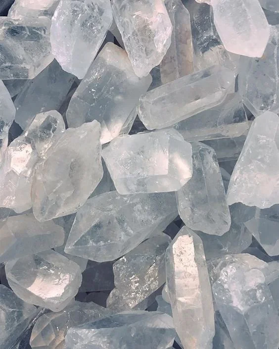 A close-up view of numerous clear quartz crystal stones of various shapes and sizes.