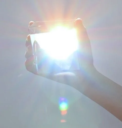 A person holding a smartphone with the sun shining directly into the camera lens, creating a bright glare and colorful lens flare.