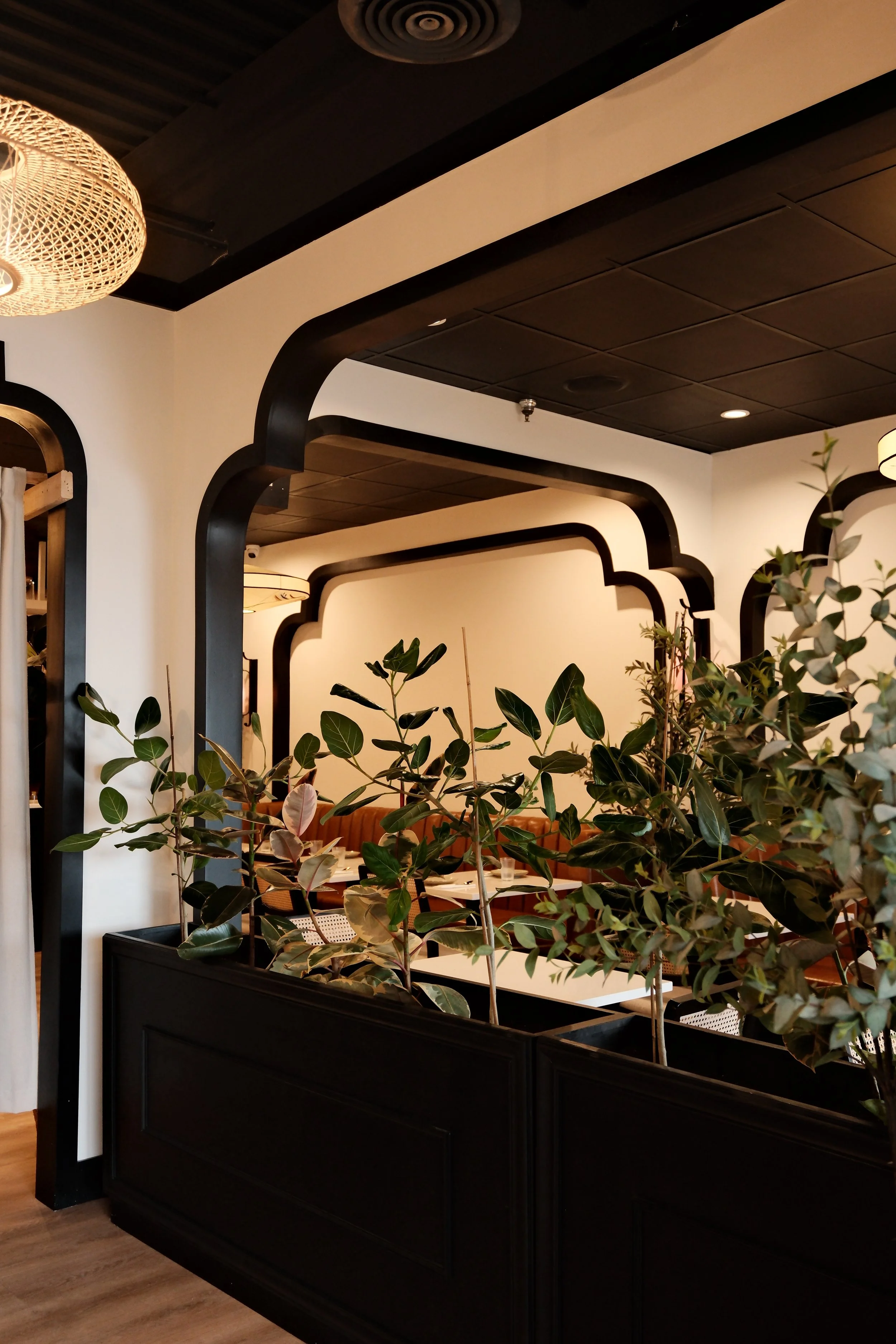 Indoor restaurant setting with dark wood accents, potted plants, and seating area visible in the background.