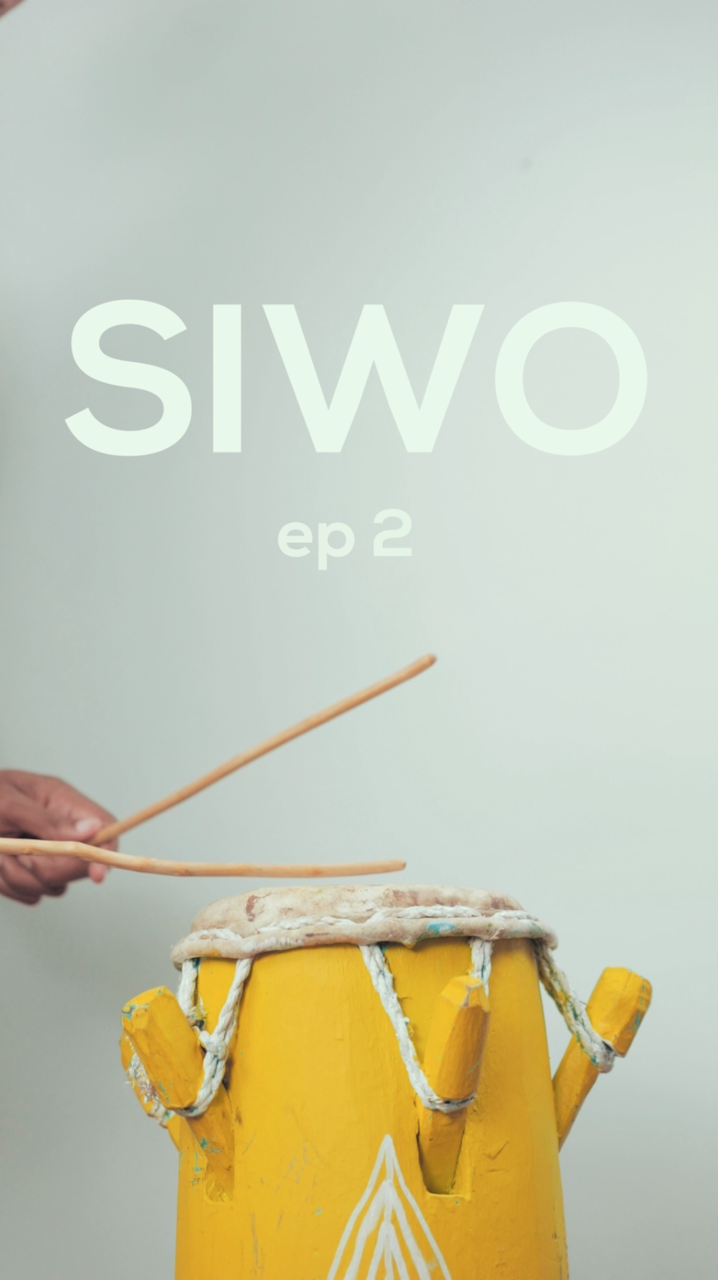 Close-up of a person holding drumsticks and playing a yellow drum with white strings on a plain light background, with the text 'SIWO ep 2' overlaid.