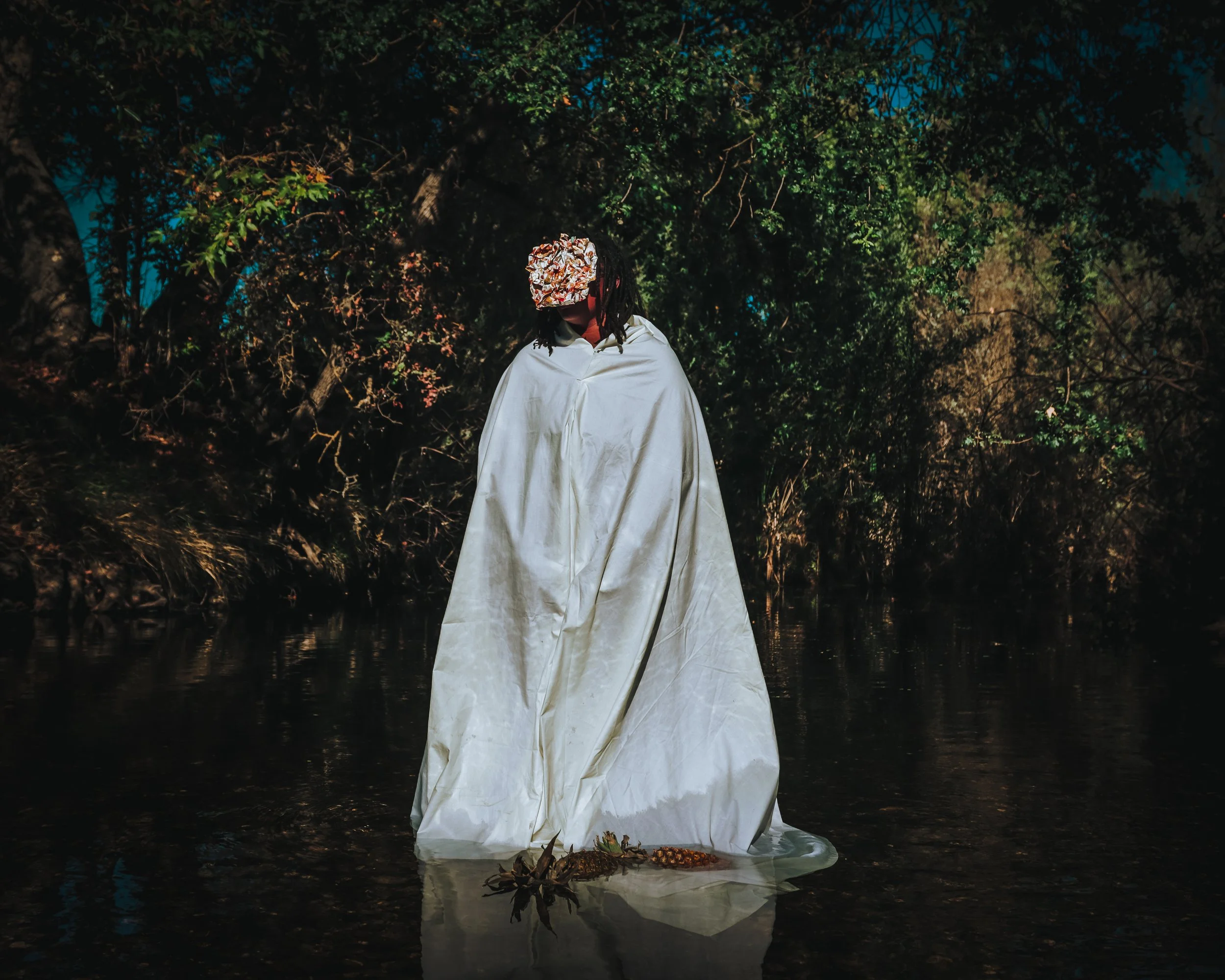 A person standing in a body of water at night, wearing a white dress and a cap made of aluminum foil, with trees in the background.