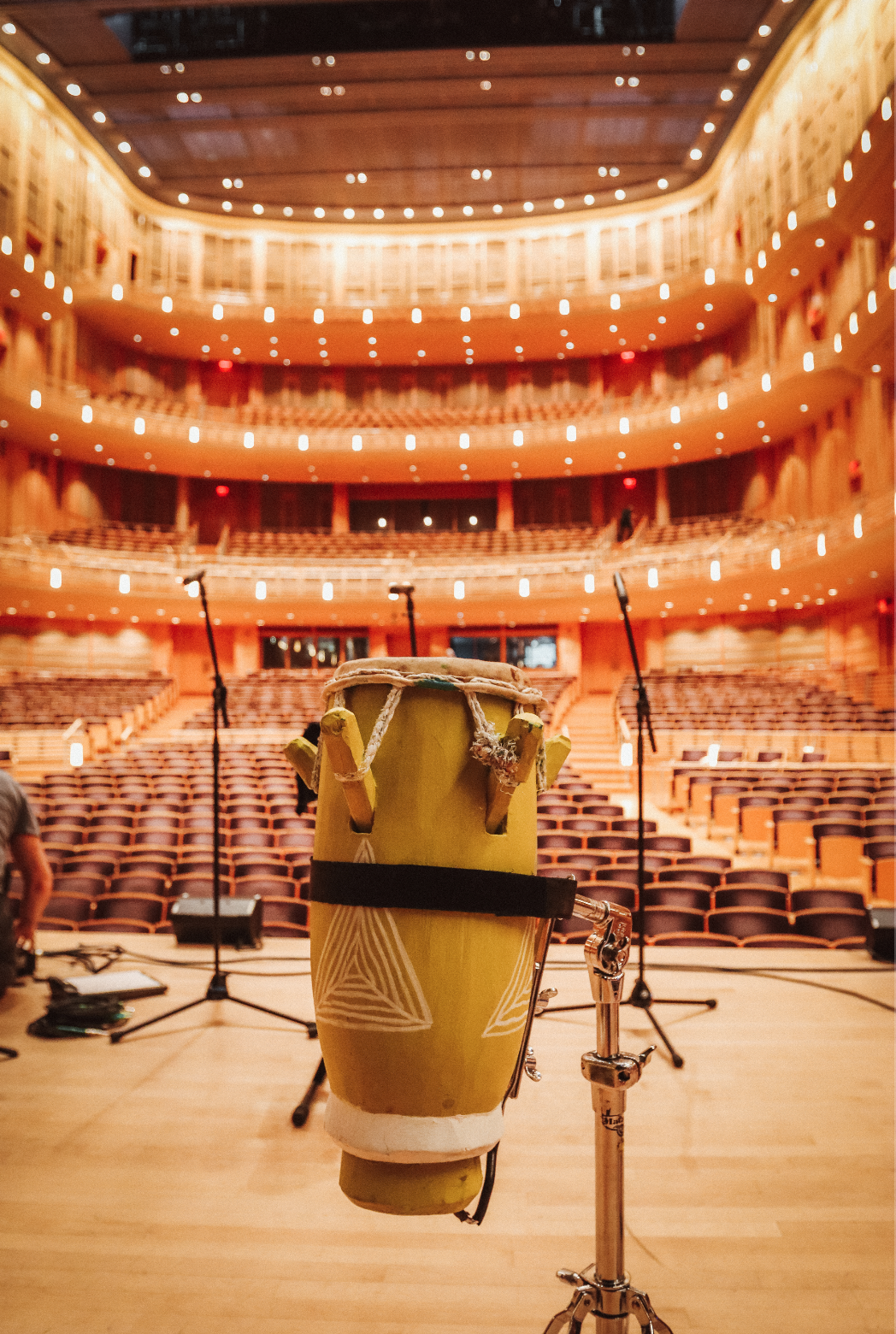 A drum on a stage in a concert hall with empty seats and lit balconies.