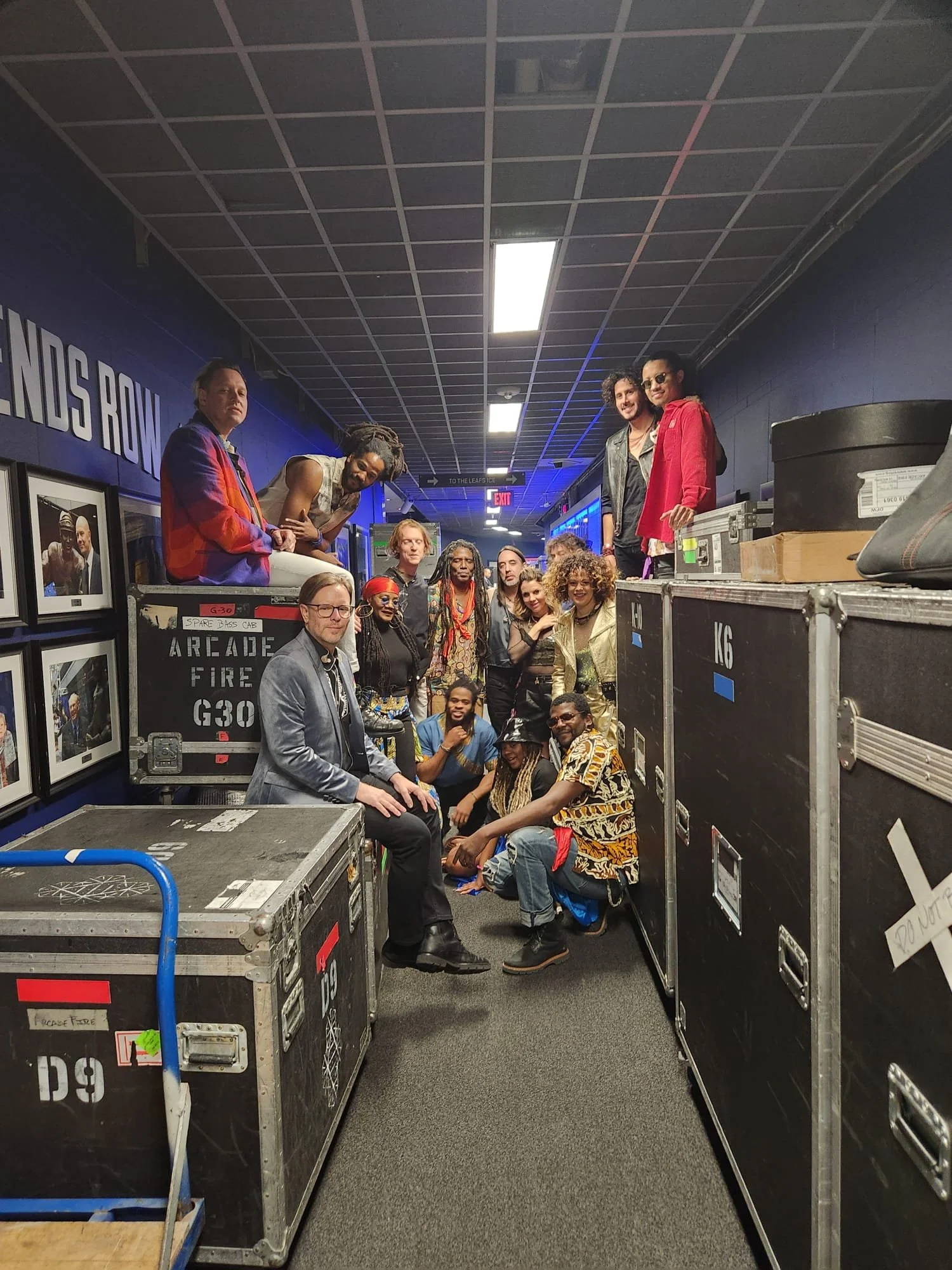 Group of people gathered in a hallway behind stage equipment cases, posing for a photo with some smiling and others making playful expressions.