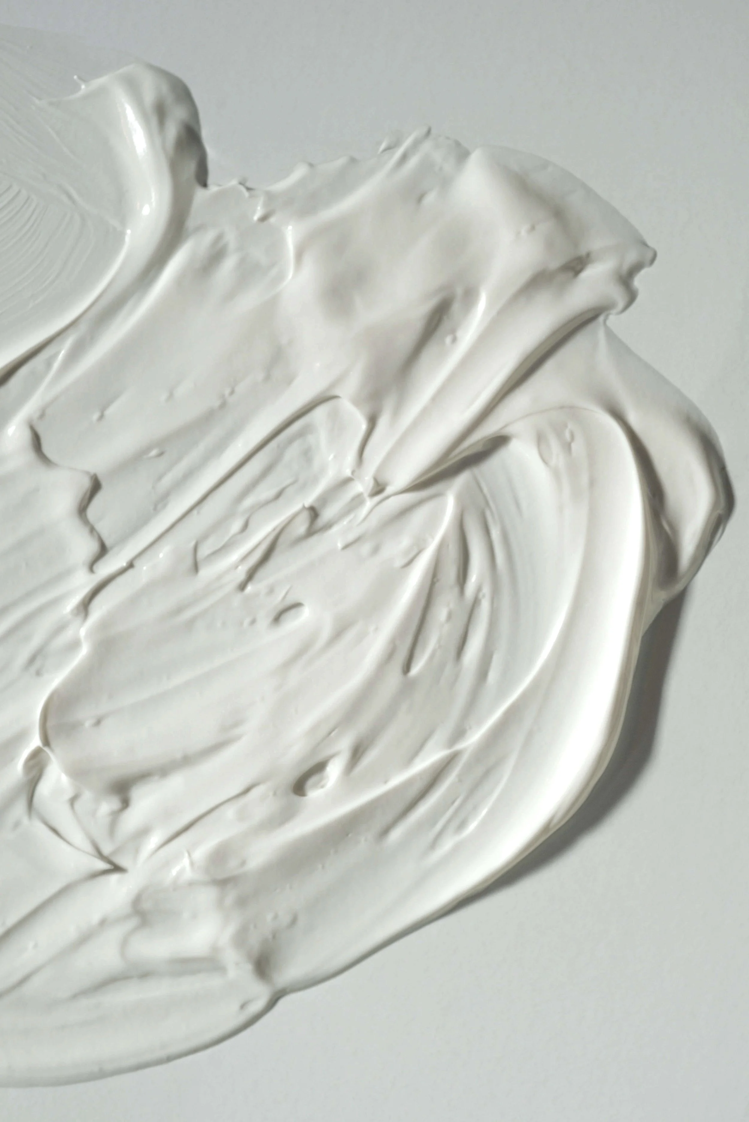 Close-up of thick, white cream or frosting spread on a surface, with textured brush strokes visible.