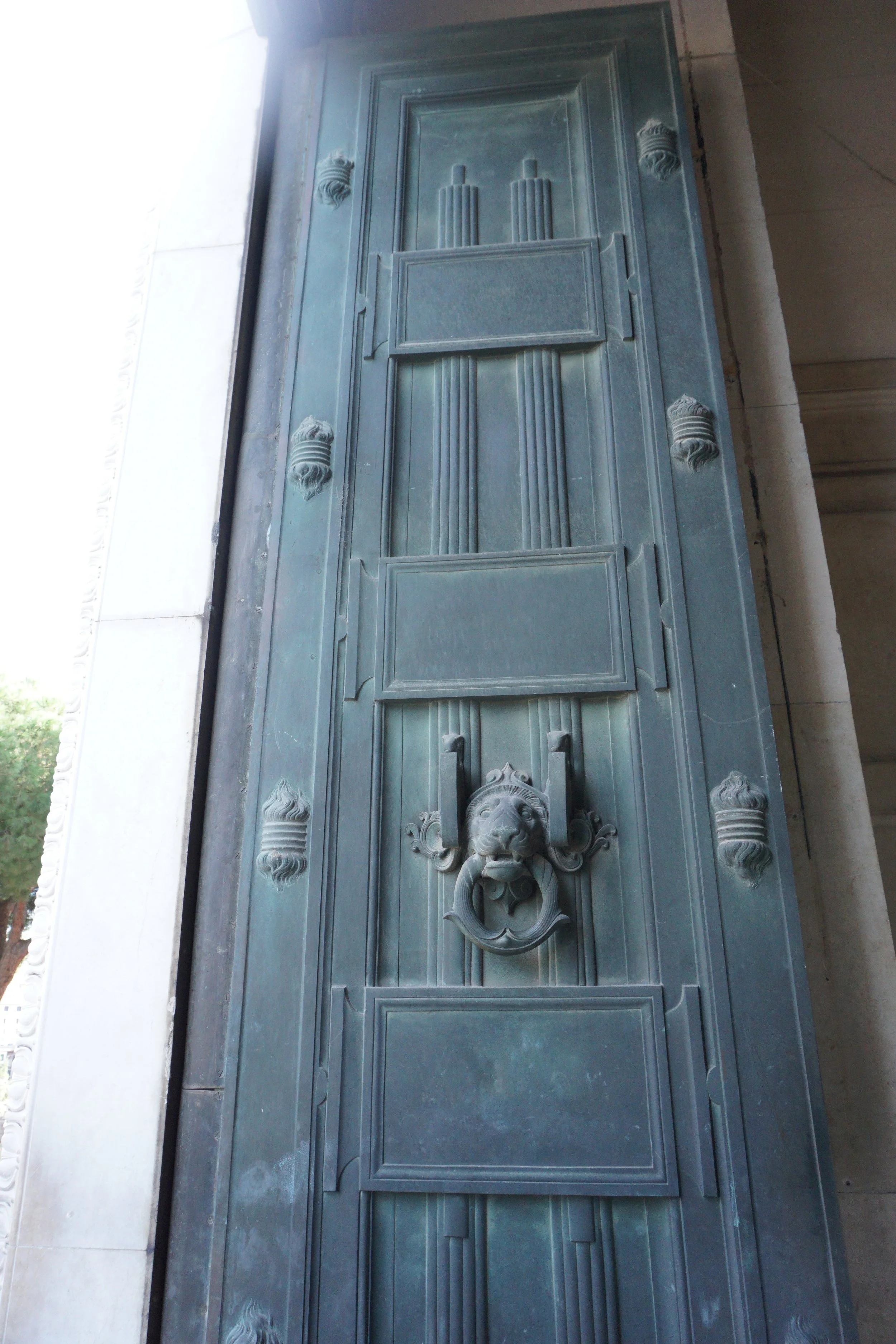 Close-up of an ornate bronze door with decorative panels, a lion head door knocker, and intricate detailing.