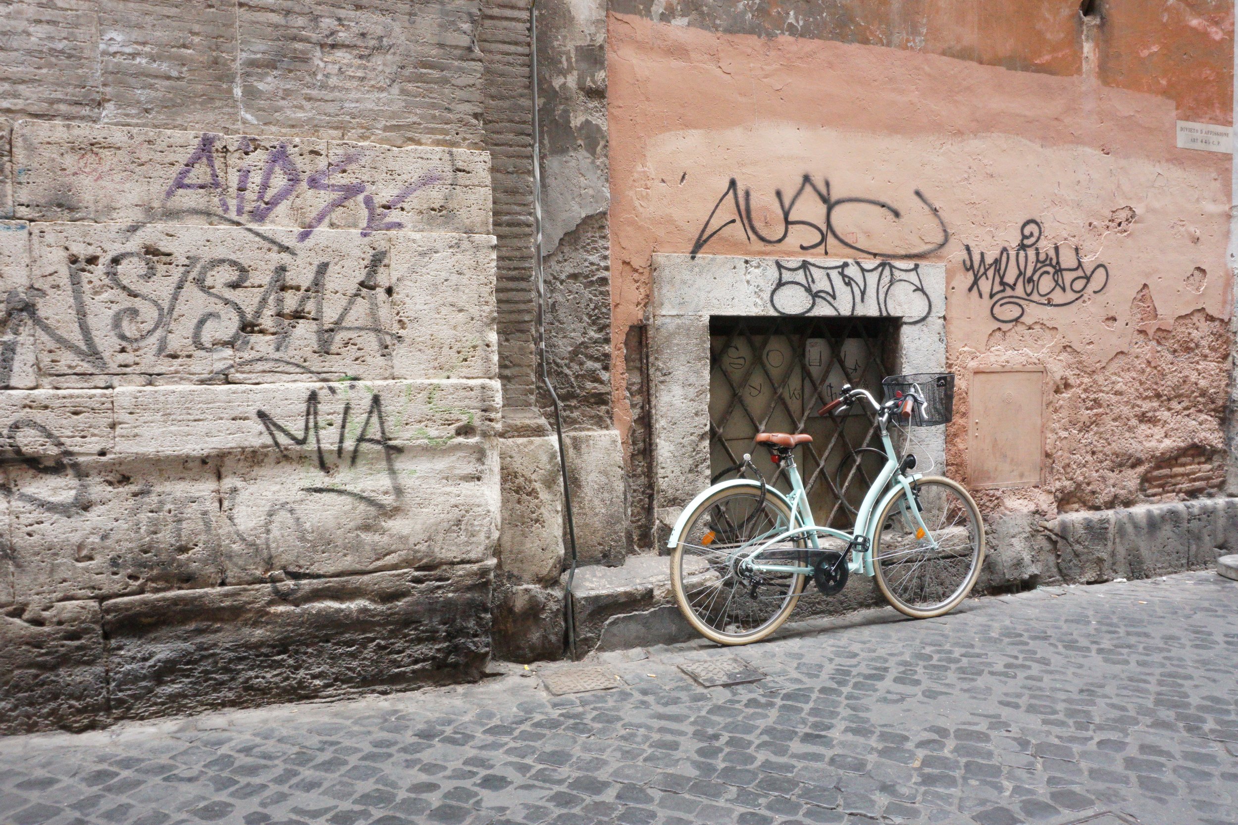 A parked bicycle leaning against a weathered wall with graffiti, cobblestone street in the foreground