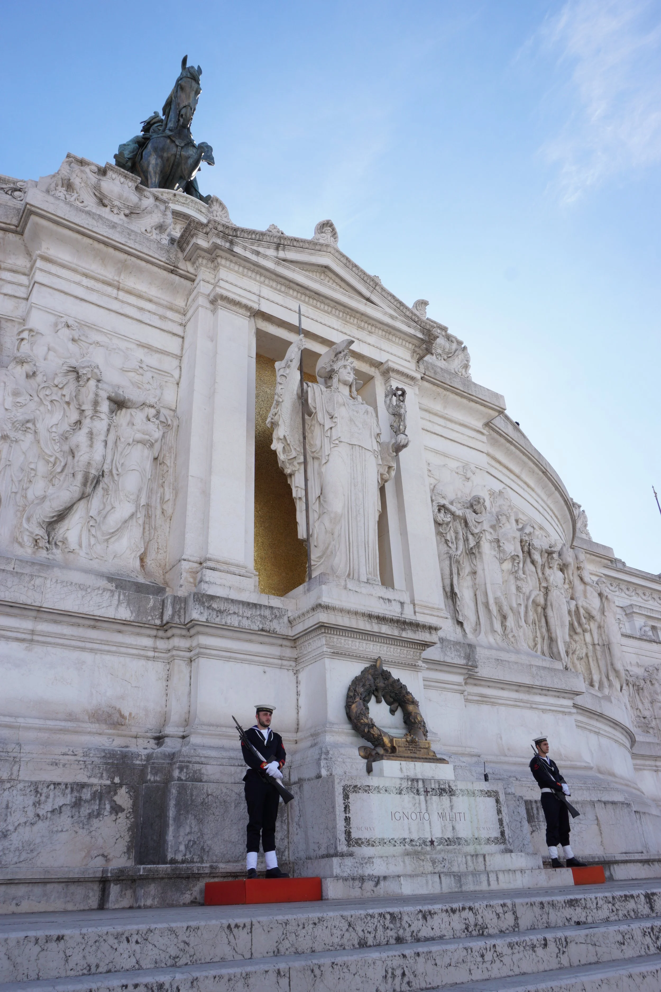 A monument with detailed carvings and sculptures, featuring two guards in uniform standing on the steps in front.