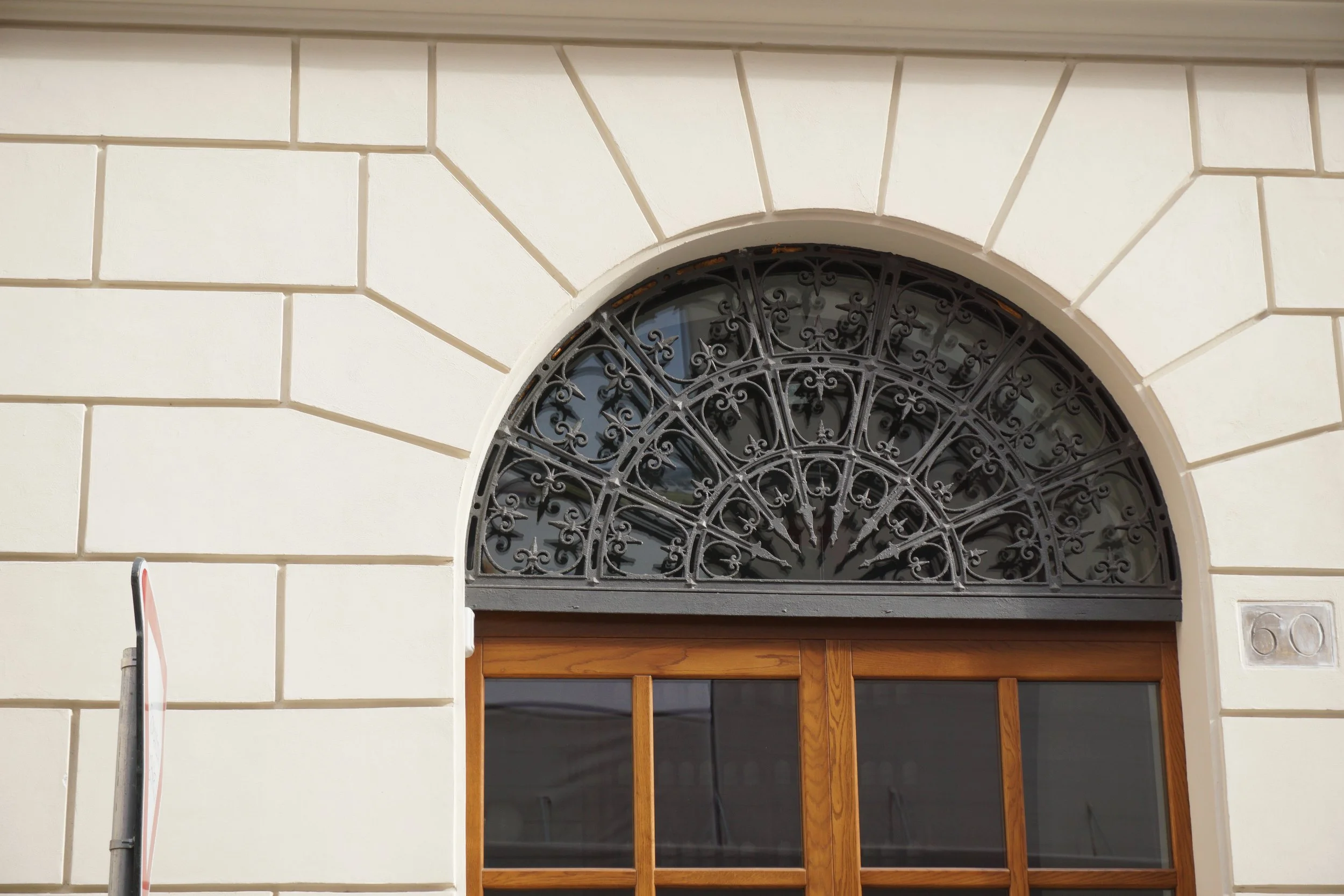 Close-up of a building's exterior wall with a decorative iron grille above a wooden door or window.