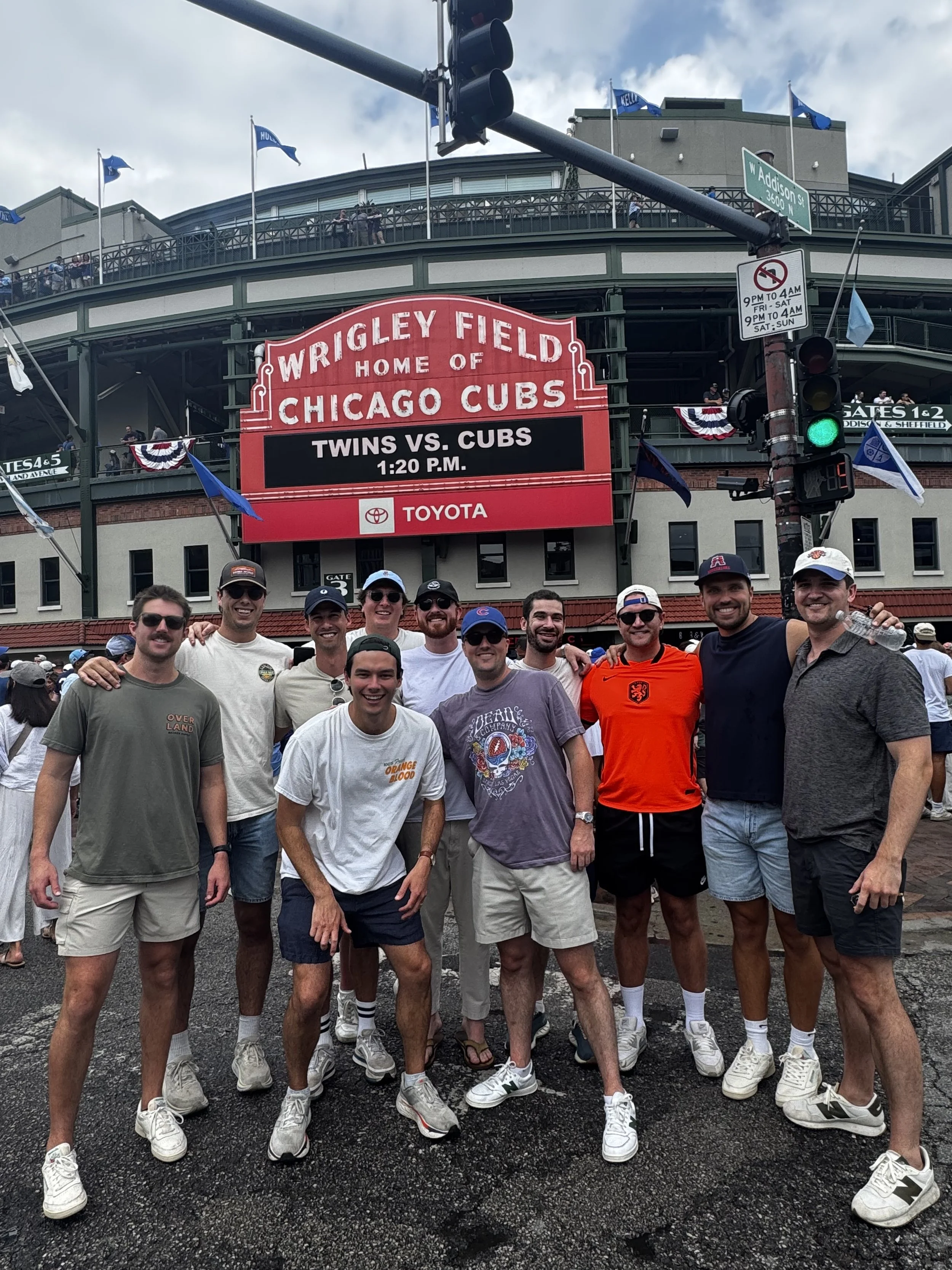 Group of eleven men posing for a photo in front of Wrigley Field stadium sign in Chicago.