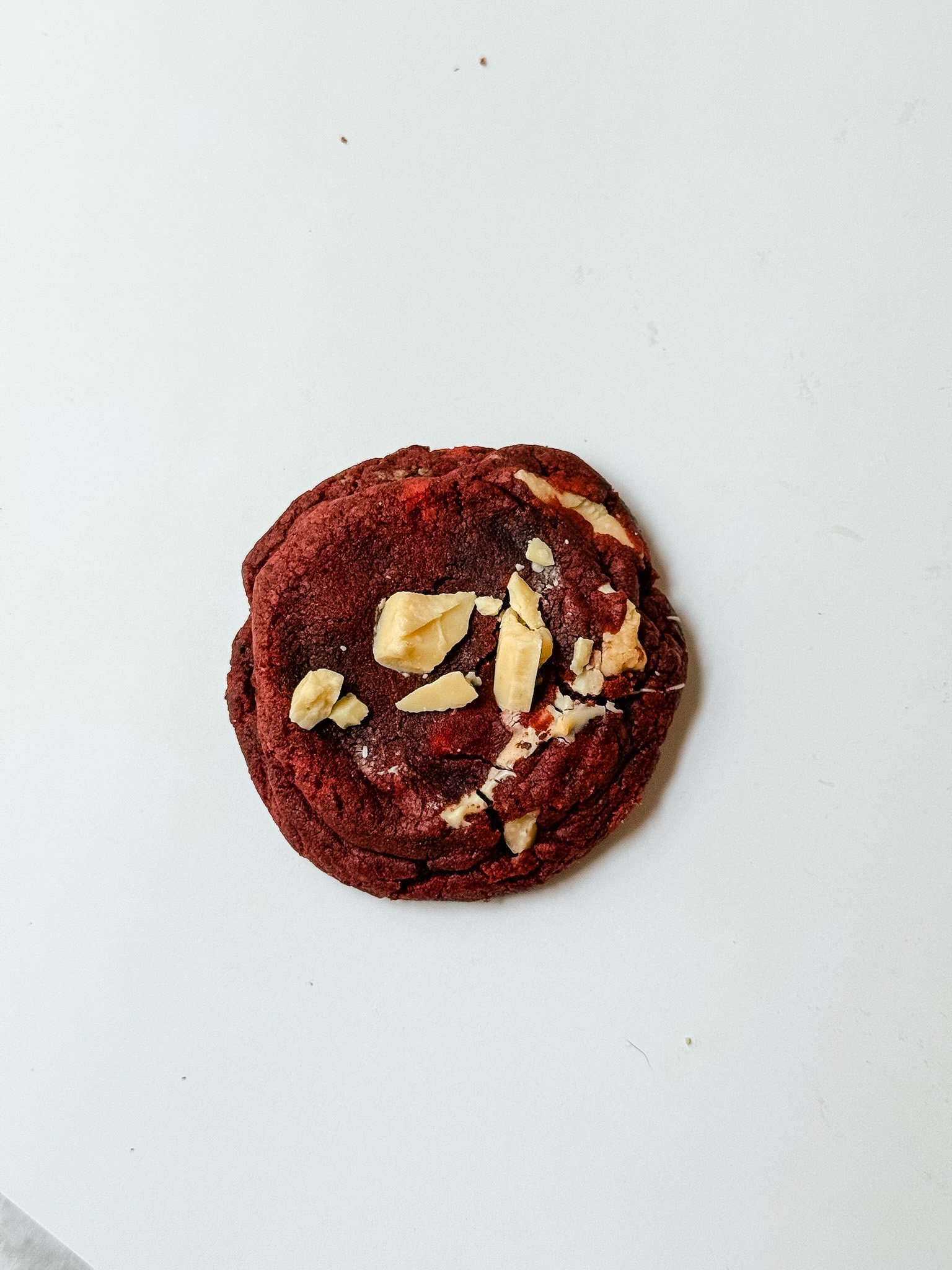 Red chocolate cookie topped with chopped almonds on a white surface.