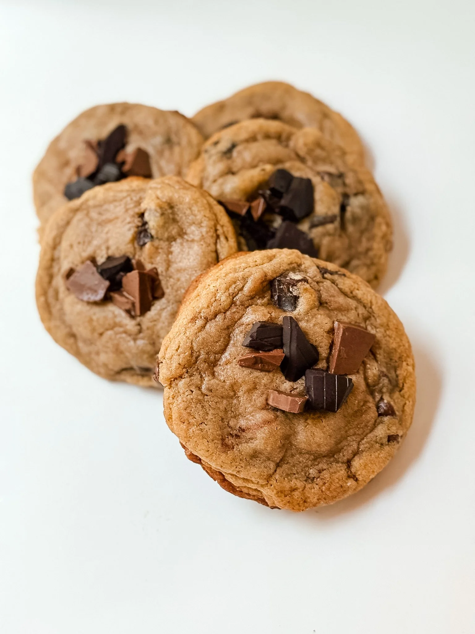 Close-up of five chocolate chip cookies stacked on a white surface.