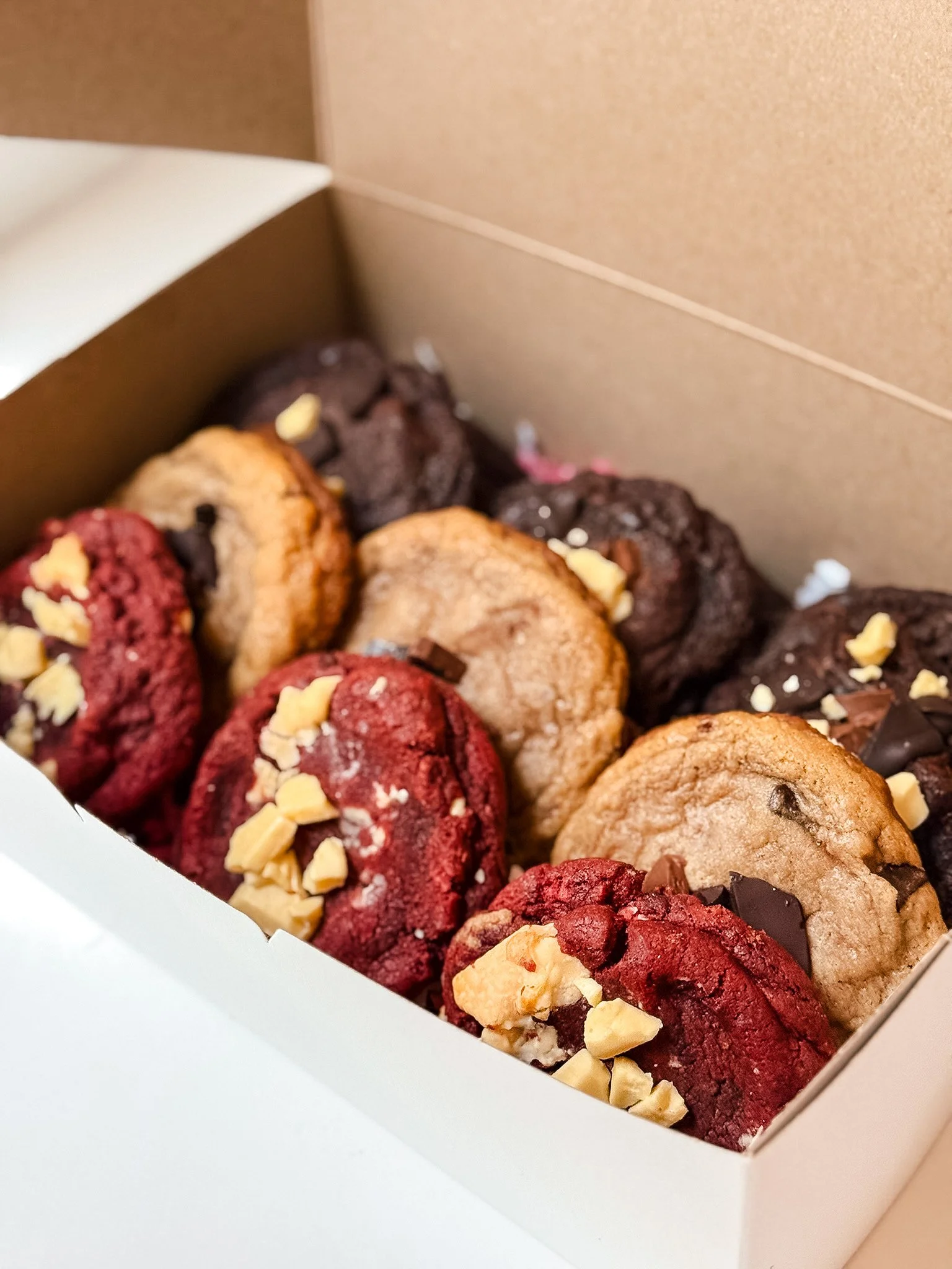 Assorted cookies topped with chopped nuts inside a white box