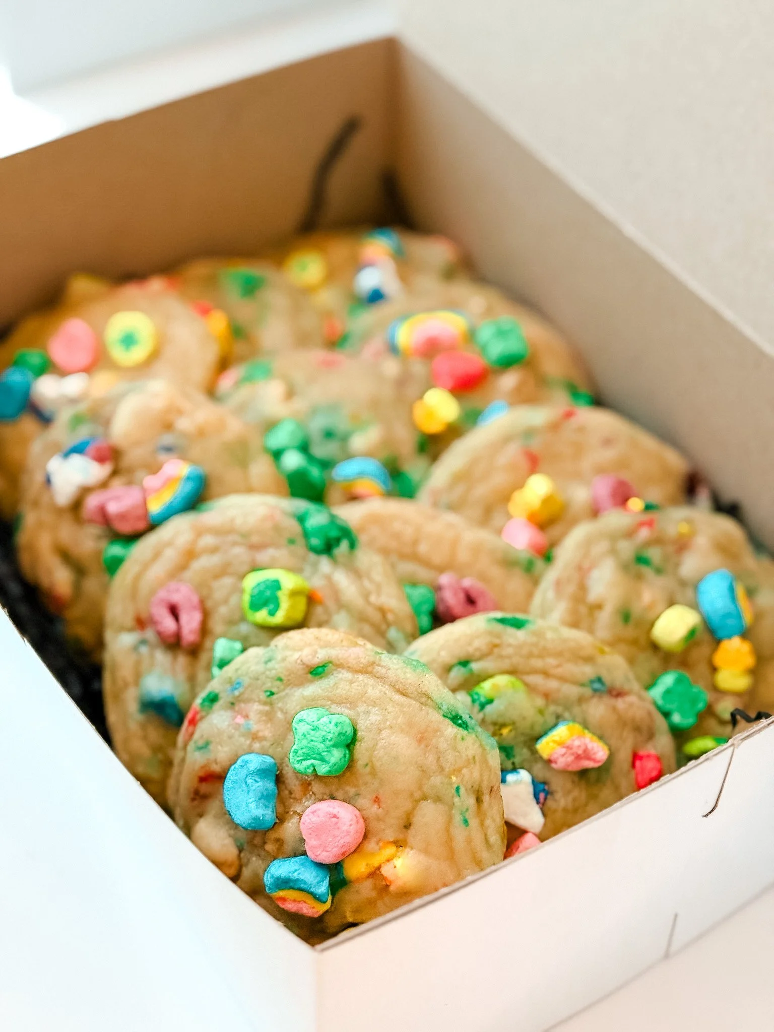 Box of sugar cookies decorated with colorful sprinkles inside a white box.