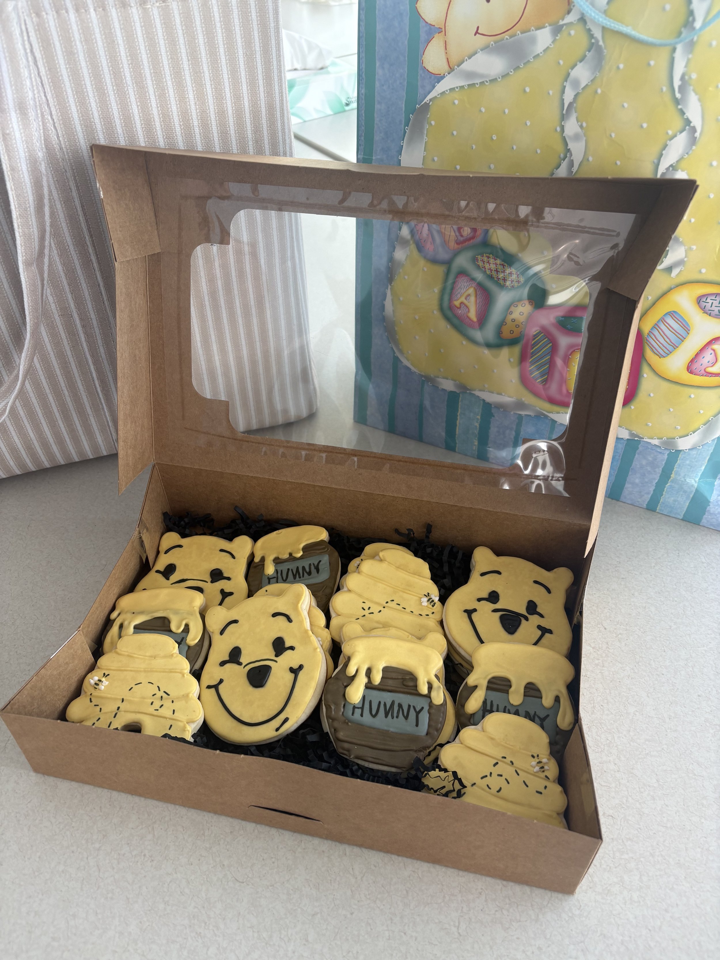 Box of decorated cookies shaped like cartoon puppy faces, some with 'HUNY' written on them, with yellow icing and black facial features.