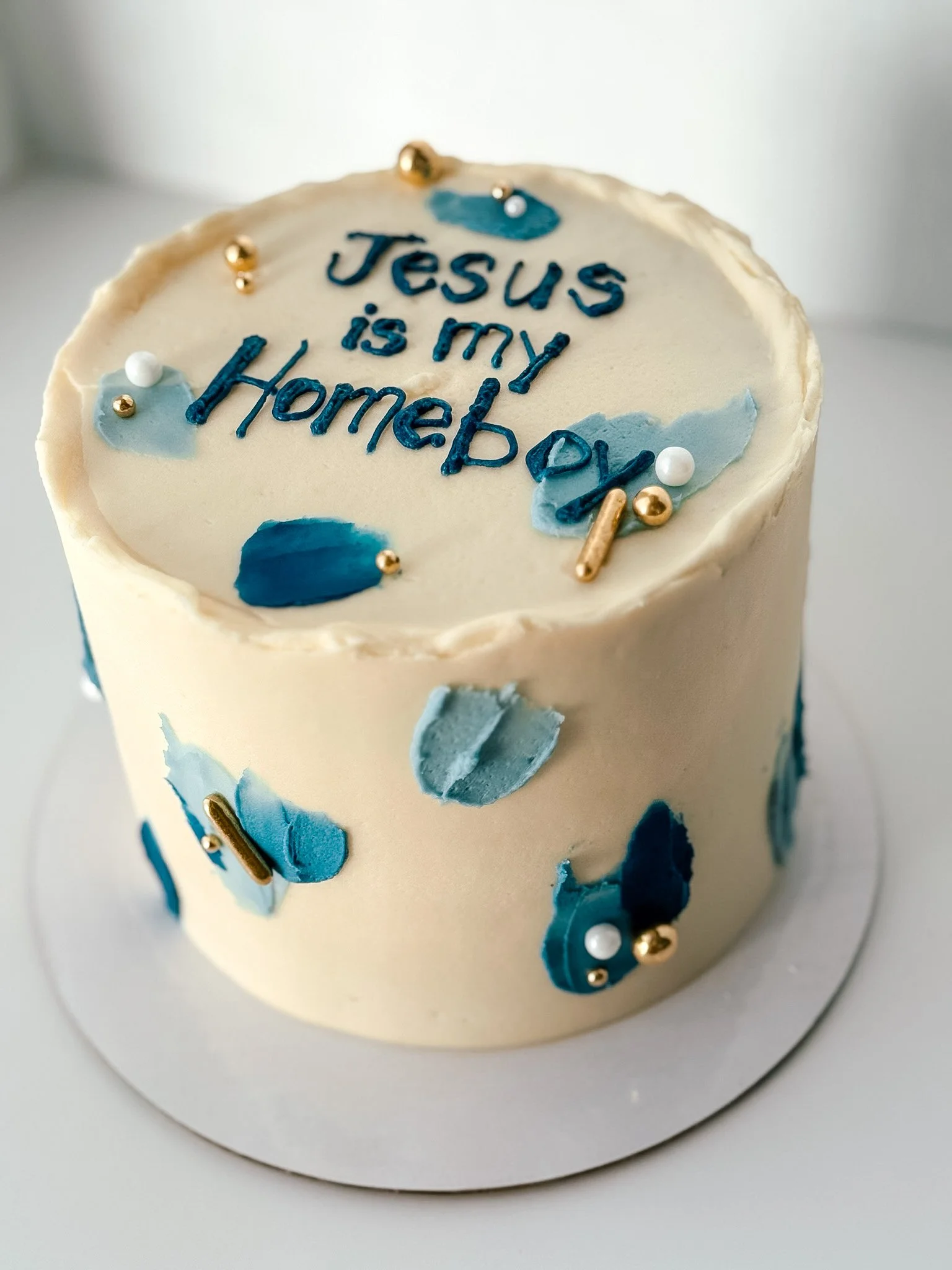 A birthday cake with white frosting decorated with blue and gold accents, and the message "Jesus is my Hobby" written on top.