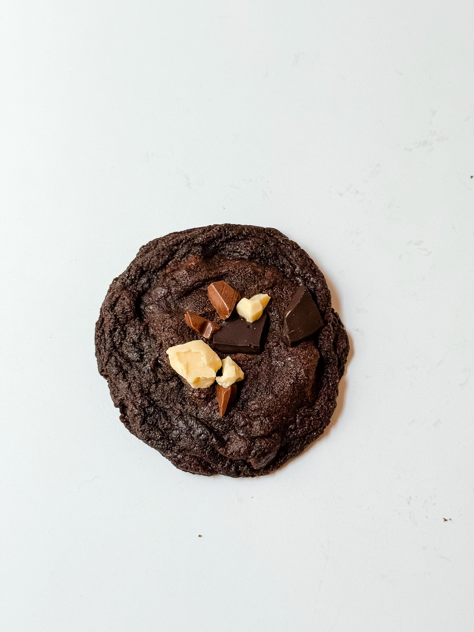 Chocolate cookie topped with various chocolate pieces and white chocolate chunks on a white background.