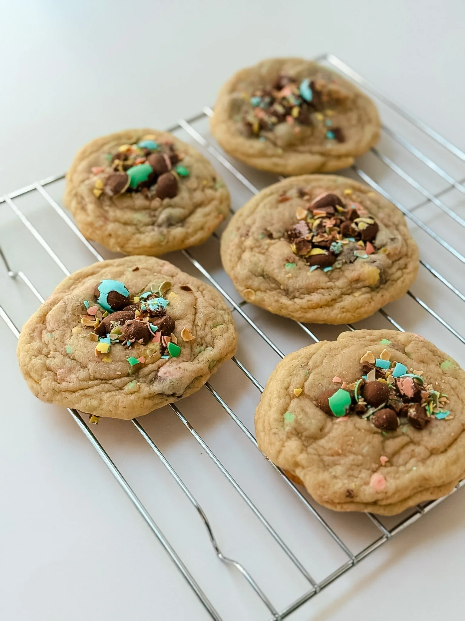 Six chocolate chip cookies with colorful sprinkles cooling on a wire rack.