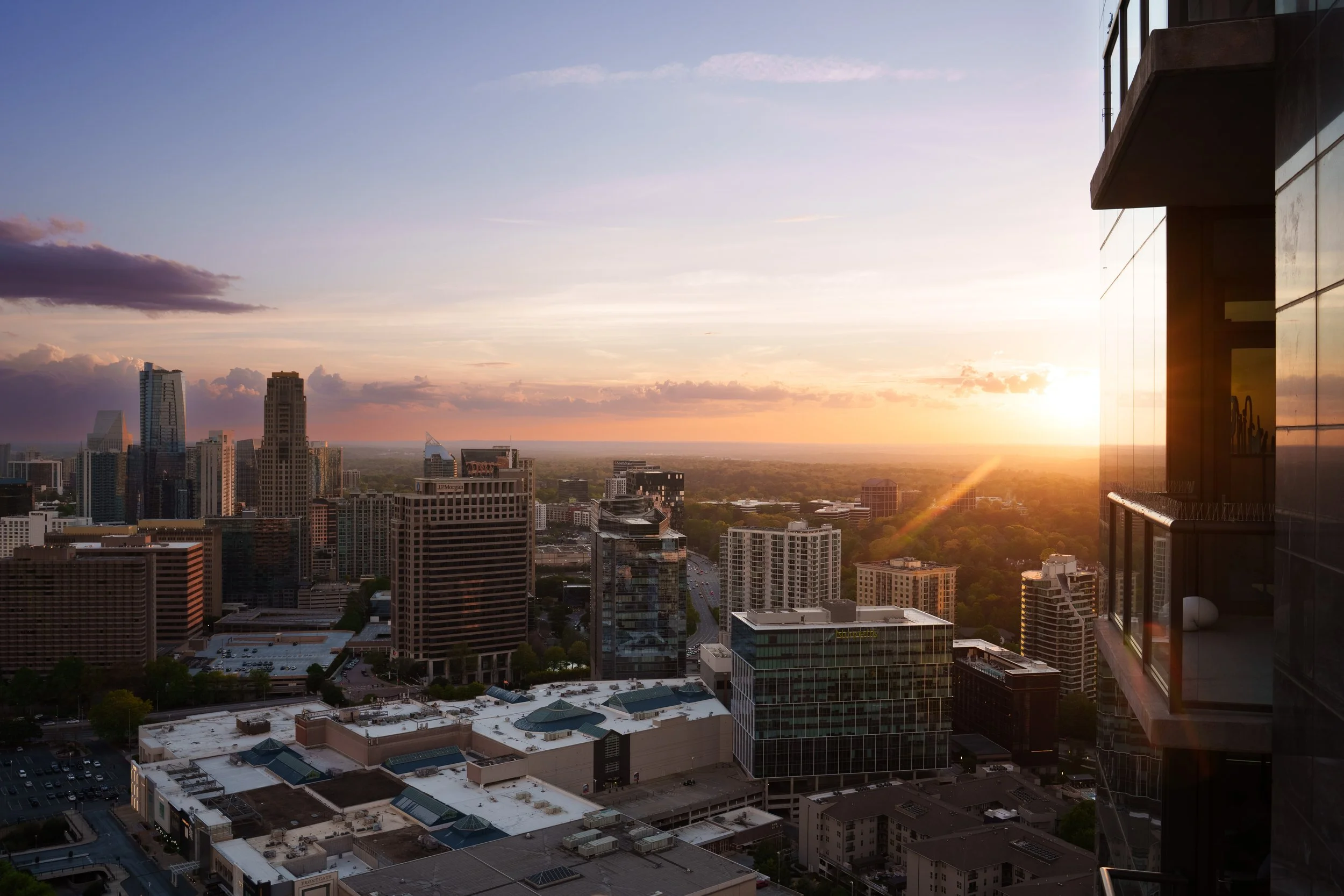 Skyline of a city during sunset with tall buildings, some with glass exteriors, and a clear sky with clouds on the horizon.