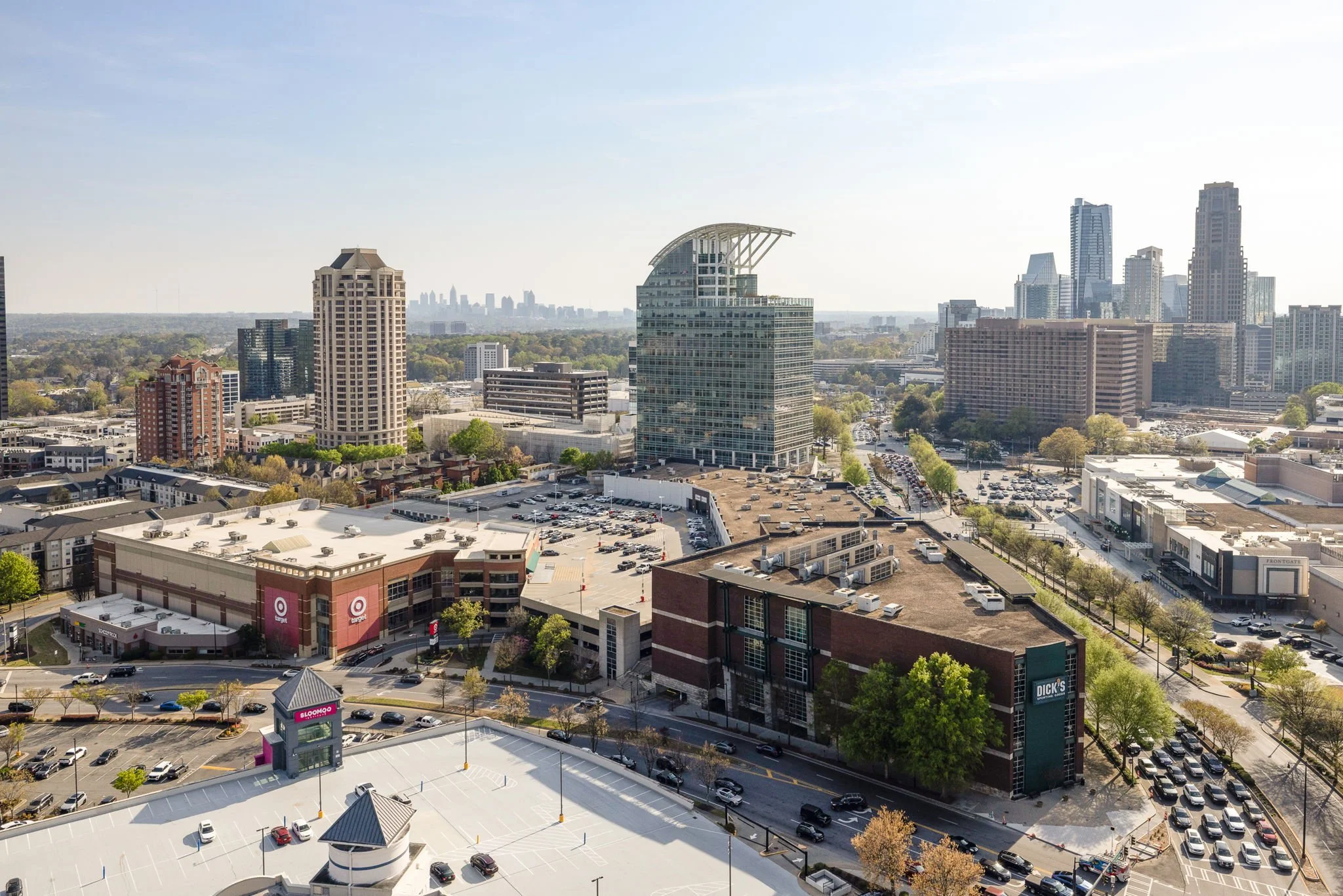 A cityscape with tall buildings, a shopping mall, parking lots, and streets lined with trees.