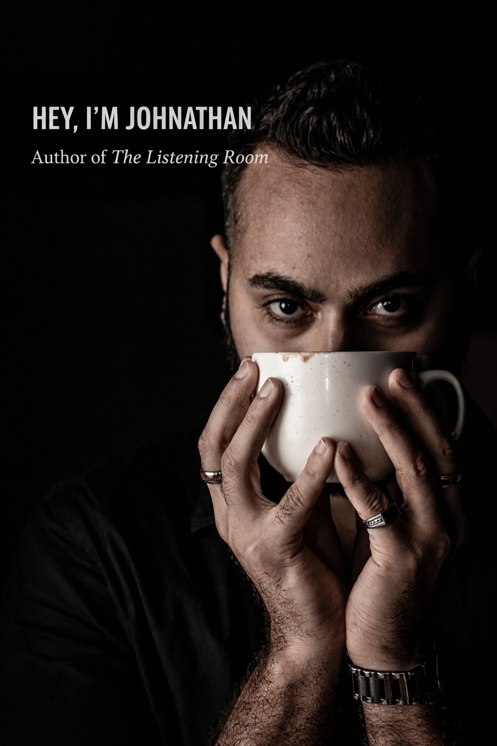 A man with dark hair and eyes holding a white coffee mug close to his face against a black background.
