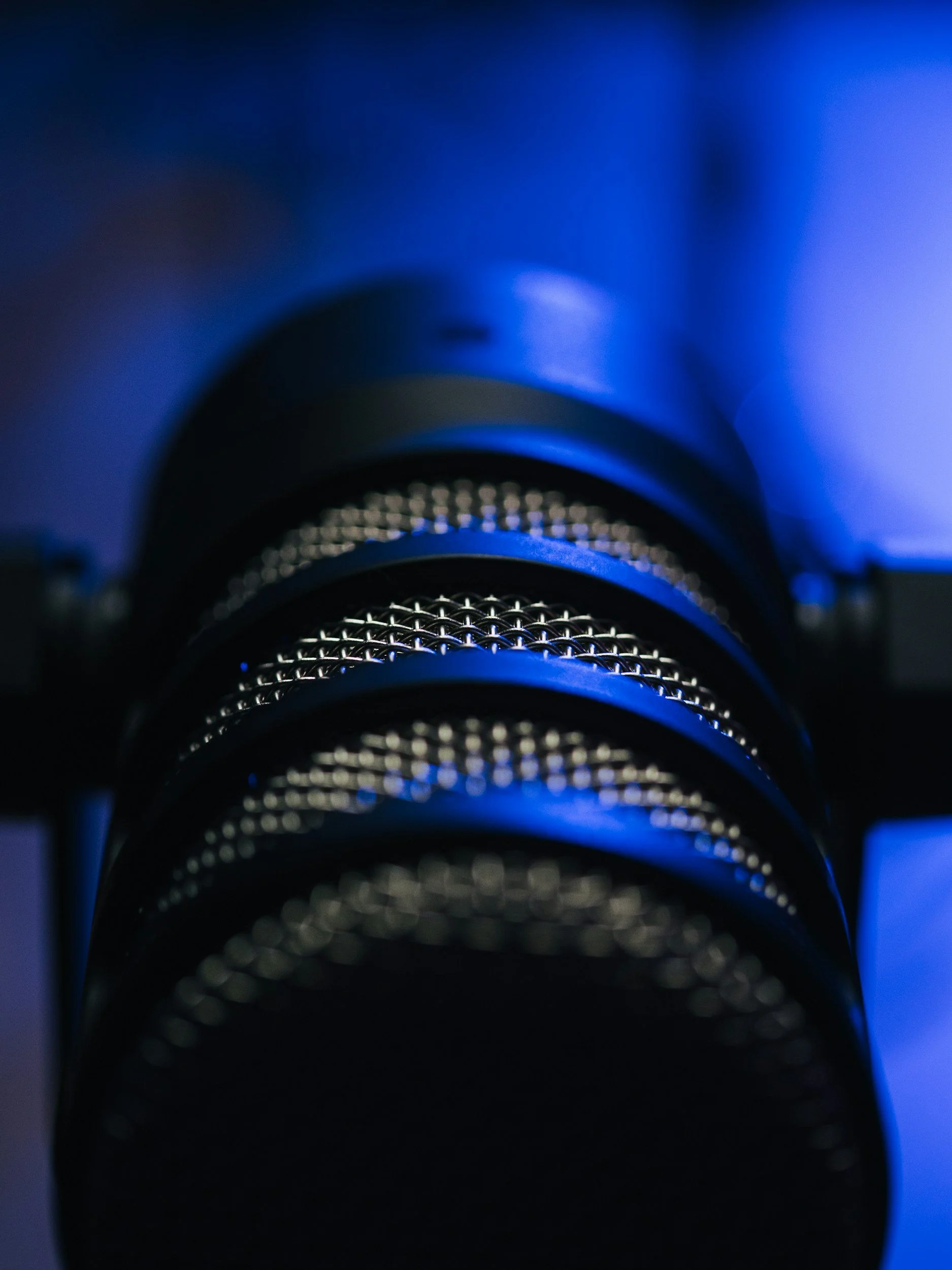 Close-up of a microphone grille with a blue and black background, illuminated by blue light.