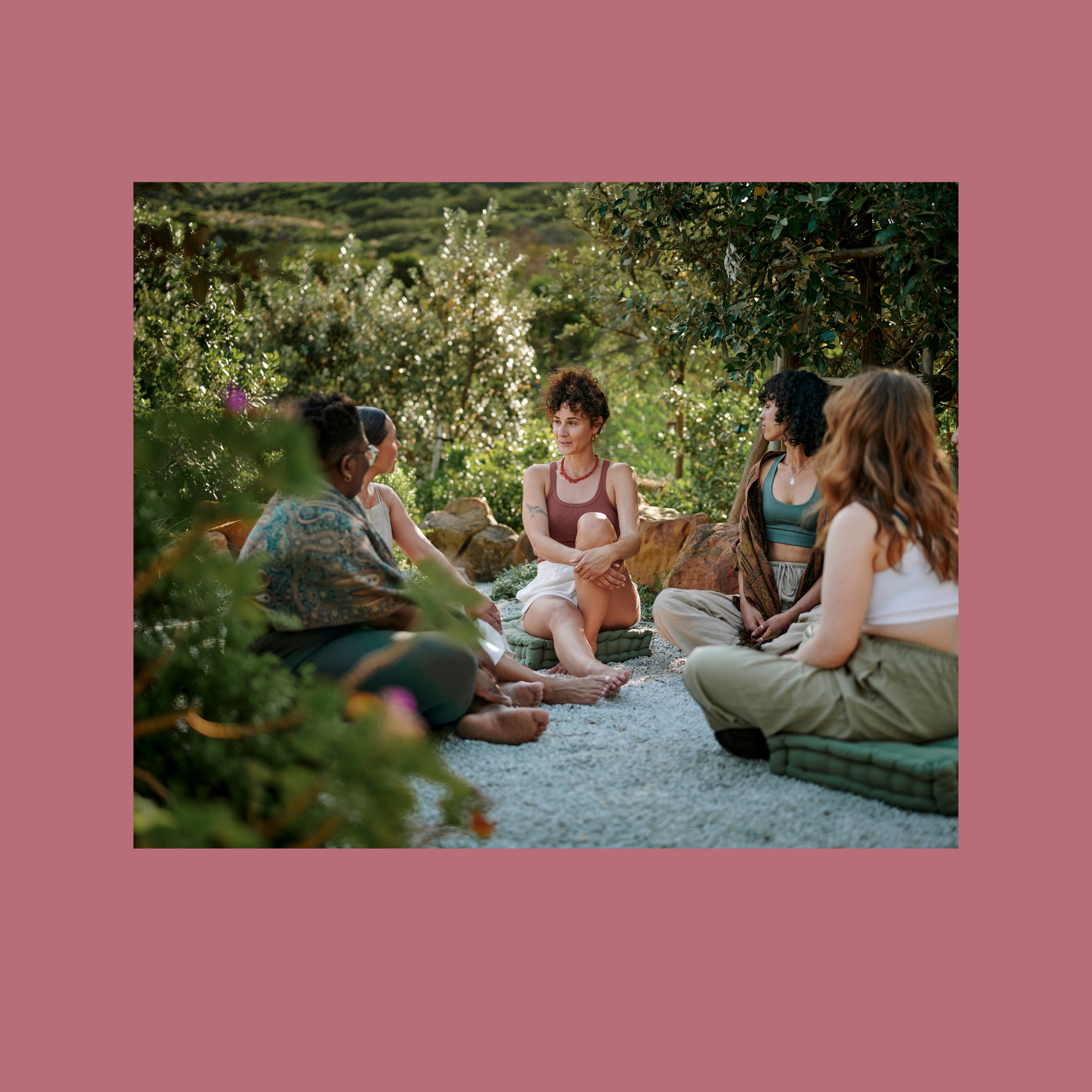 Group of diverse women sitting outdoors in a circle, engaging in conversation in a lush garden setting.