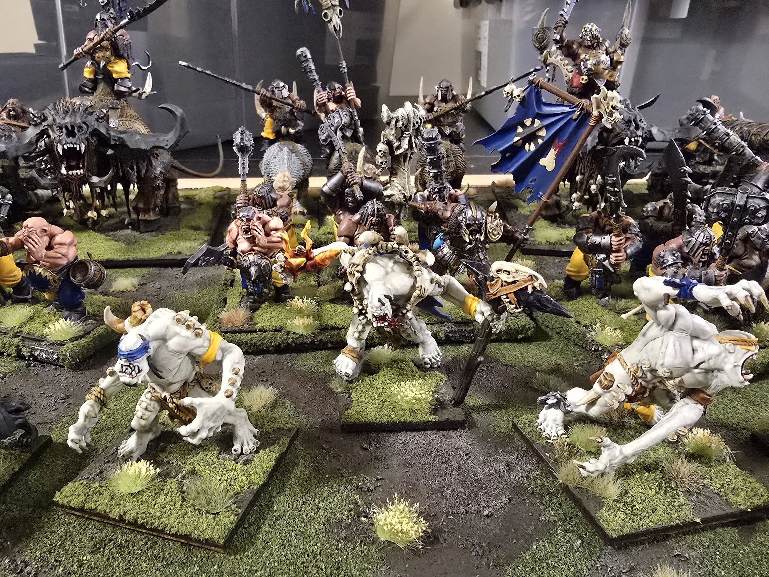 Warhammer Ogre Kingdoms models. Three pale ogres in the front of the image, with an army of ogres and beasts behind them