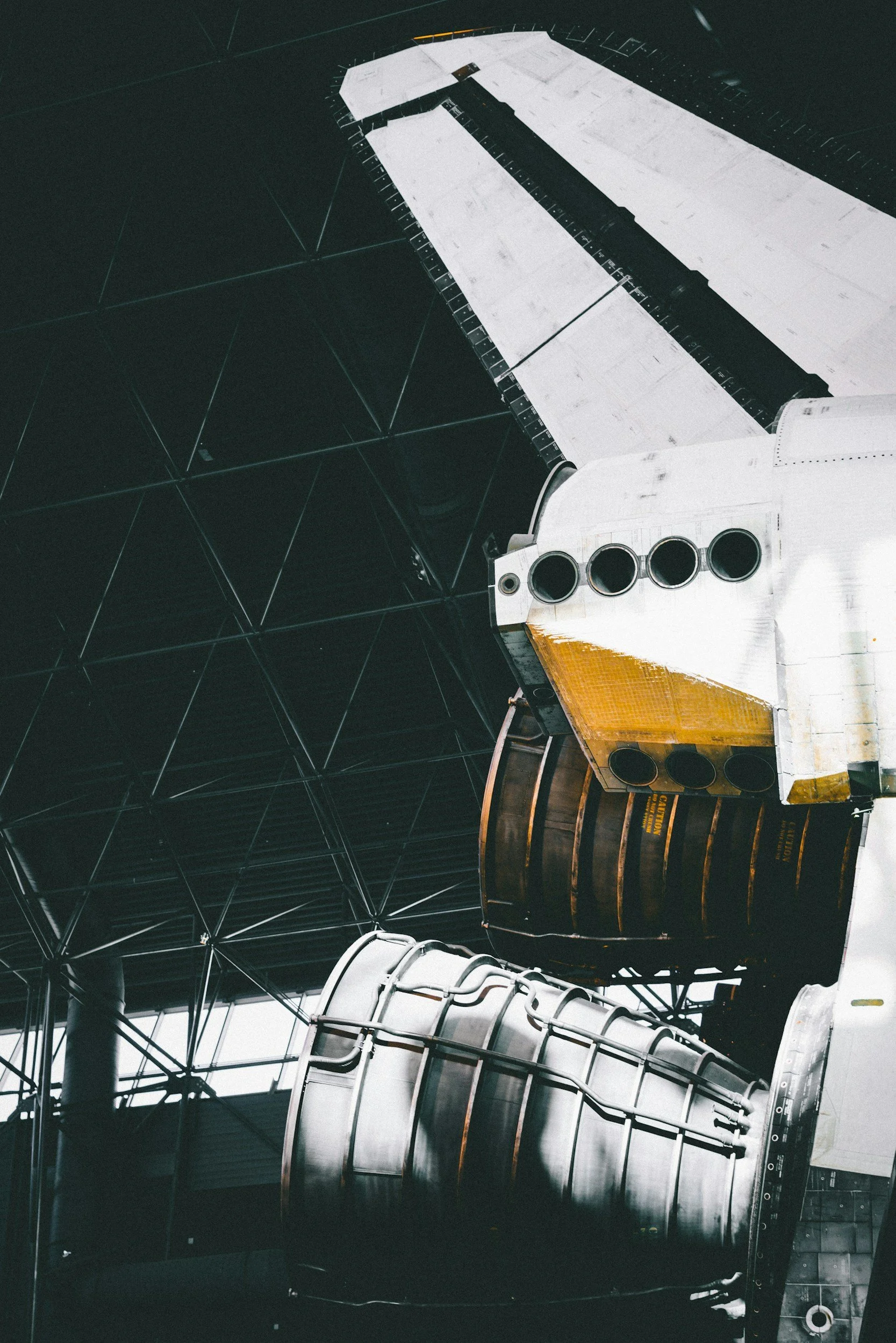 Close-up of a space shuttle's engine section inside a modern building or hangar.