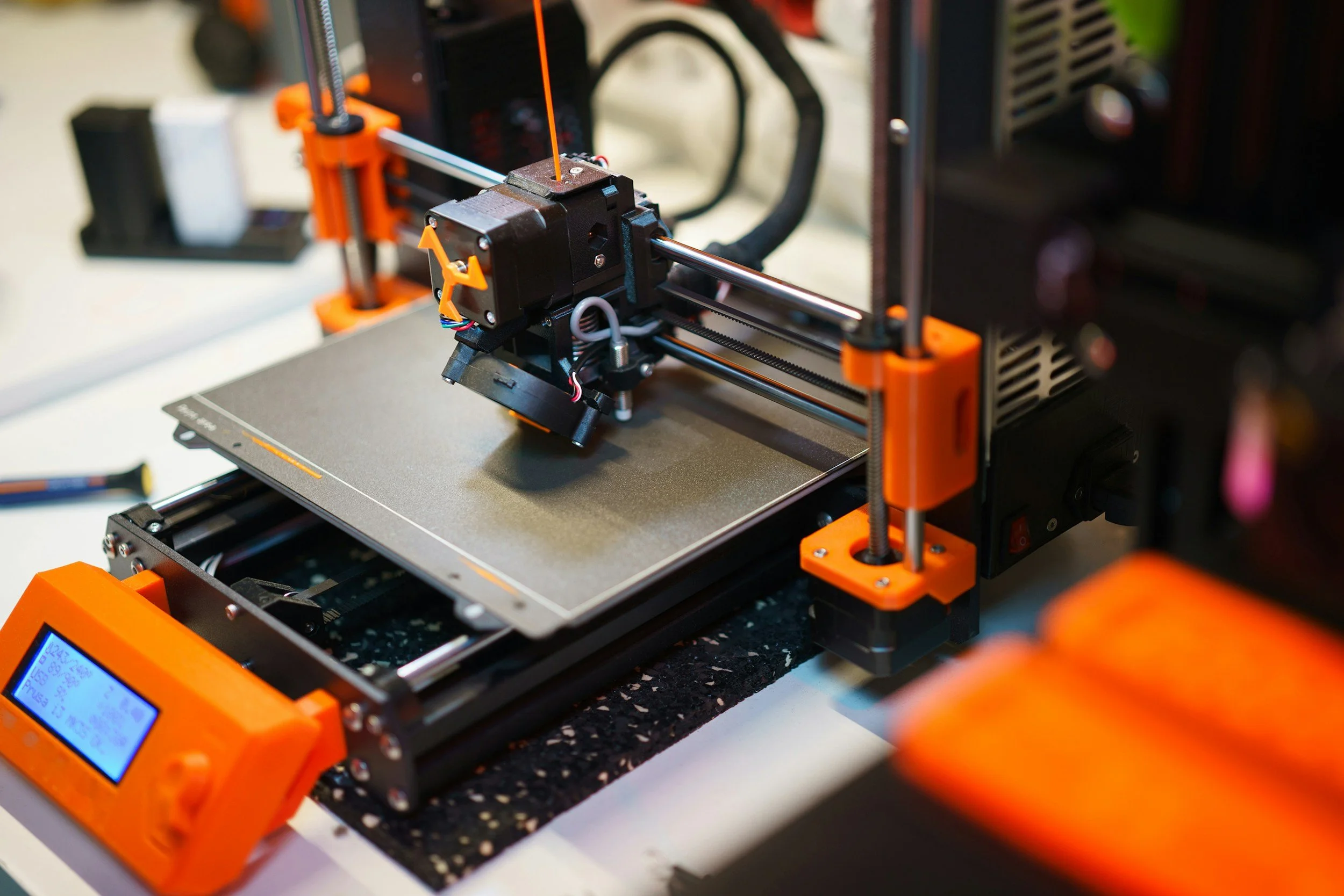 A 3D printer with orange accents printing an object on a platform.