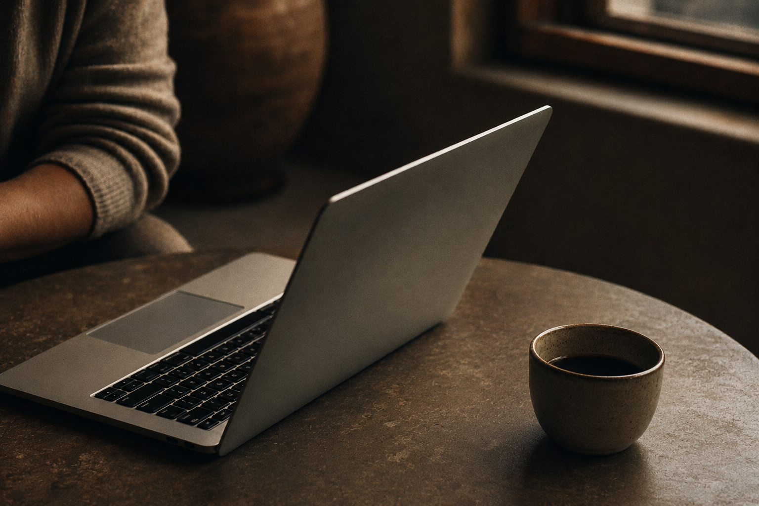 Open MacBook beside a ceramic cup of coffee in warm, low light.