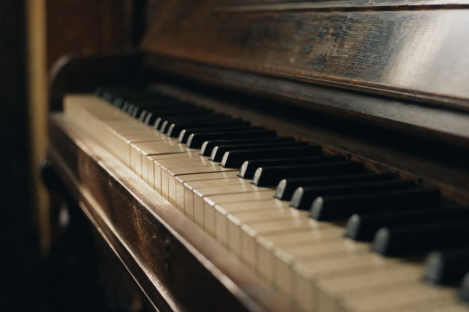 Angled view of the keys on a dark wooden upright piano.
